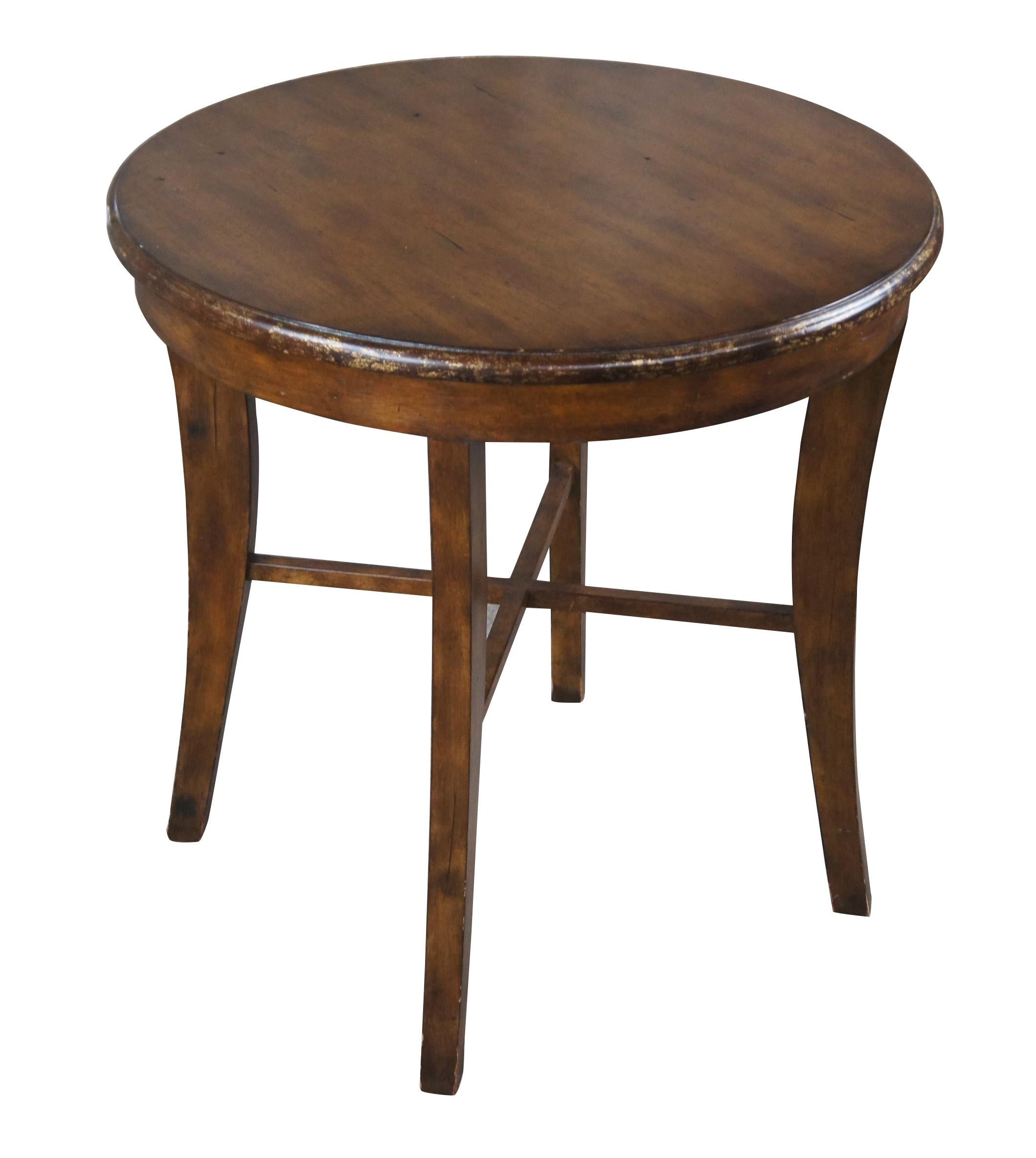 Vintage mahogany finished  center or accent table featuring round form with an antiqued rubbed gold paint edge over four legs connected by x support and slightly flared legs.

Dimensions:
27