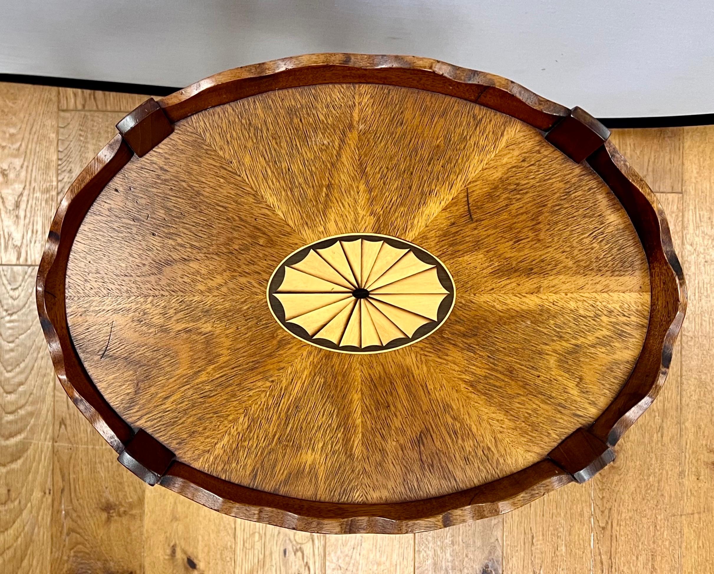 Stunning mahogany inlay table with scalloped edges.  Features oval inlay design in center and bellflower inlay on all four legs.  Rests on four brass castors for ease of movement.