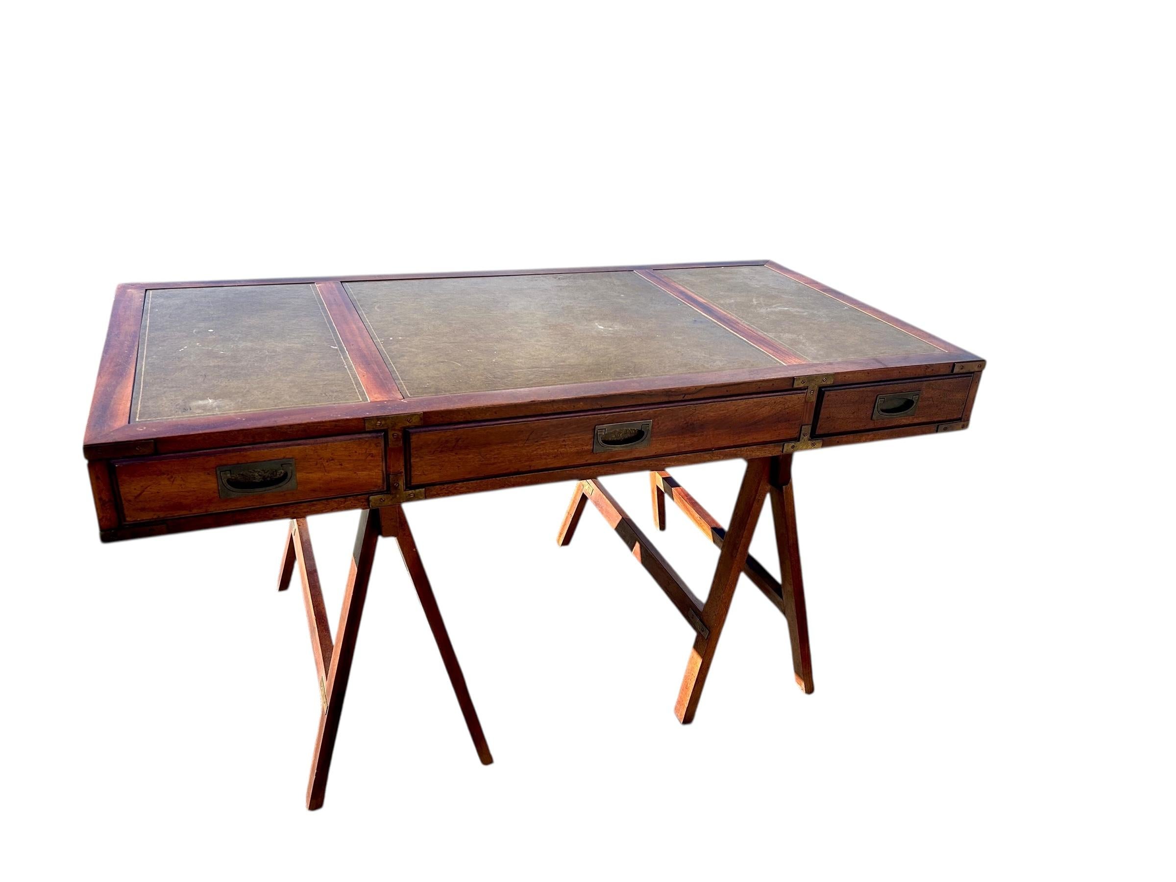 Bellissima scrivania in stile British Colonial della metà del secolo, realizzata in mogano con un piano in pelle verde lavorata in tre segmenti. Il piano presenta un lungo cassetto affiancato da due cassetti più piccoli, rifiniti con ferramenta in