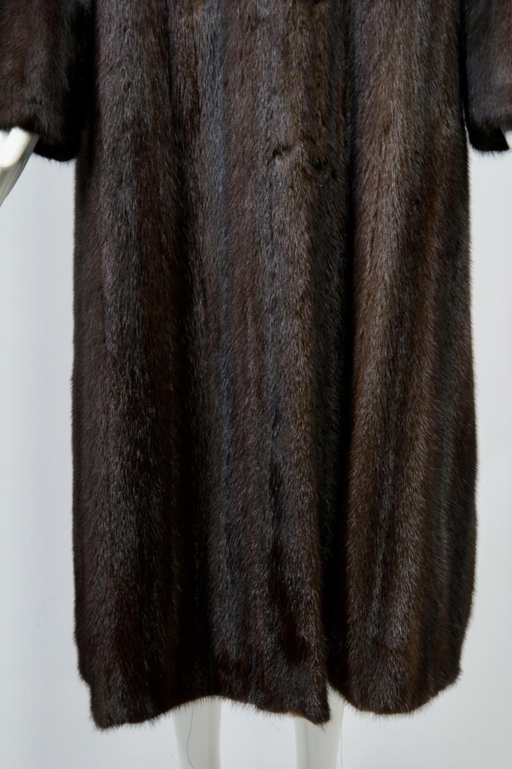 Vintage mink coat, late 20th century, in dark brown, mahogany color. The coat features a simple, straight silhouette with a notched collar, square shoulders, straight sleeves, and hidden slash pockets. Fur hook closures reinforce the clean lines of