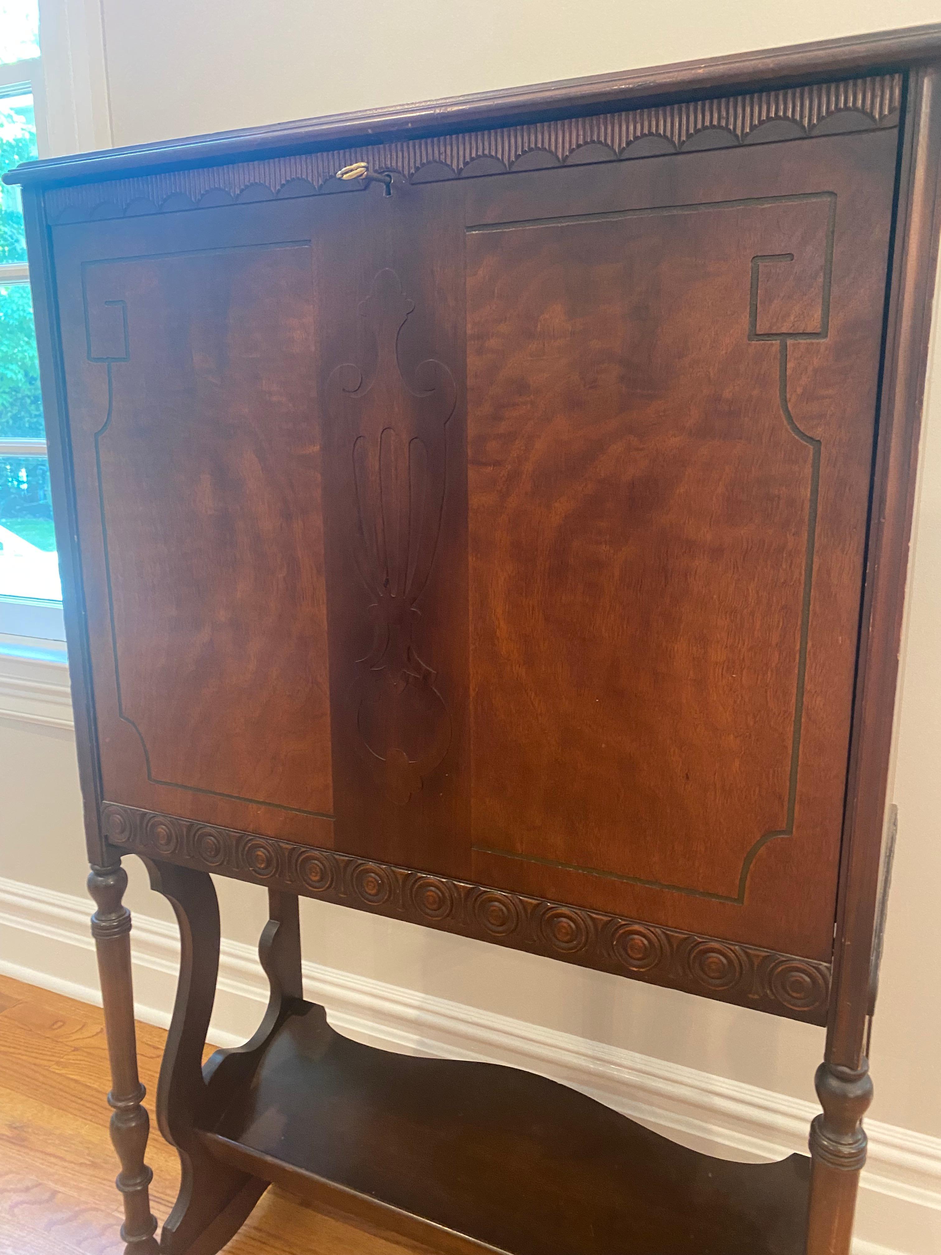 Vintage wood tall secretary having pretty flat front with carved wood decoration and urn shape in the center. Lovely grain and particularly narrow depth. Turned legs have a lower tier for more storage. The front flips down to reveal a desk surface