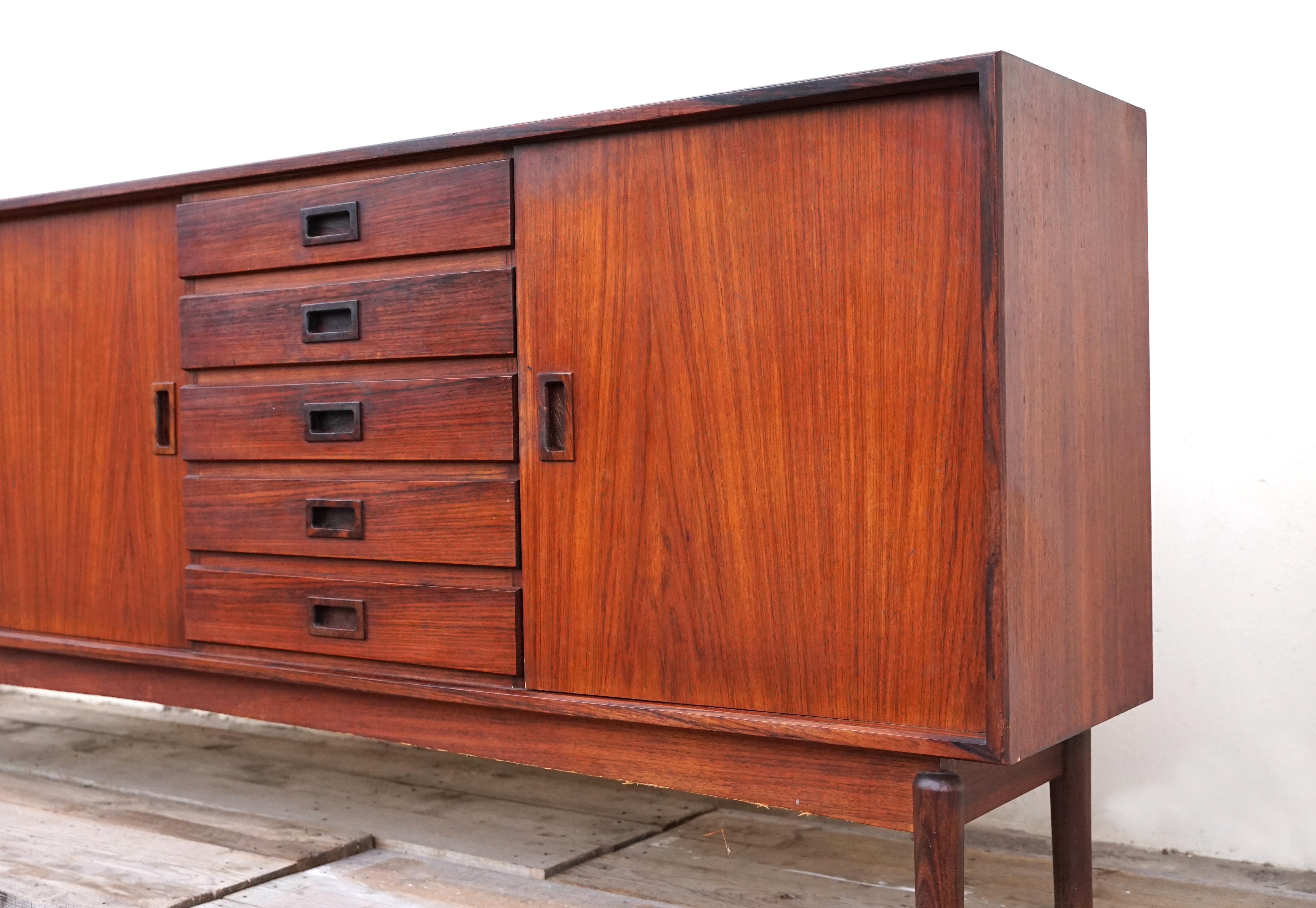 Our beautiful sideboard made of rosewood is ideal for use as a storage unit. It has two sliding doors, a chest of drawers with 5 drawers and a door that can be opened. Its vintage style and simple, sober lines will add a unique design touch to your