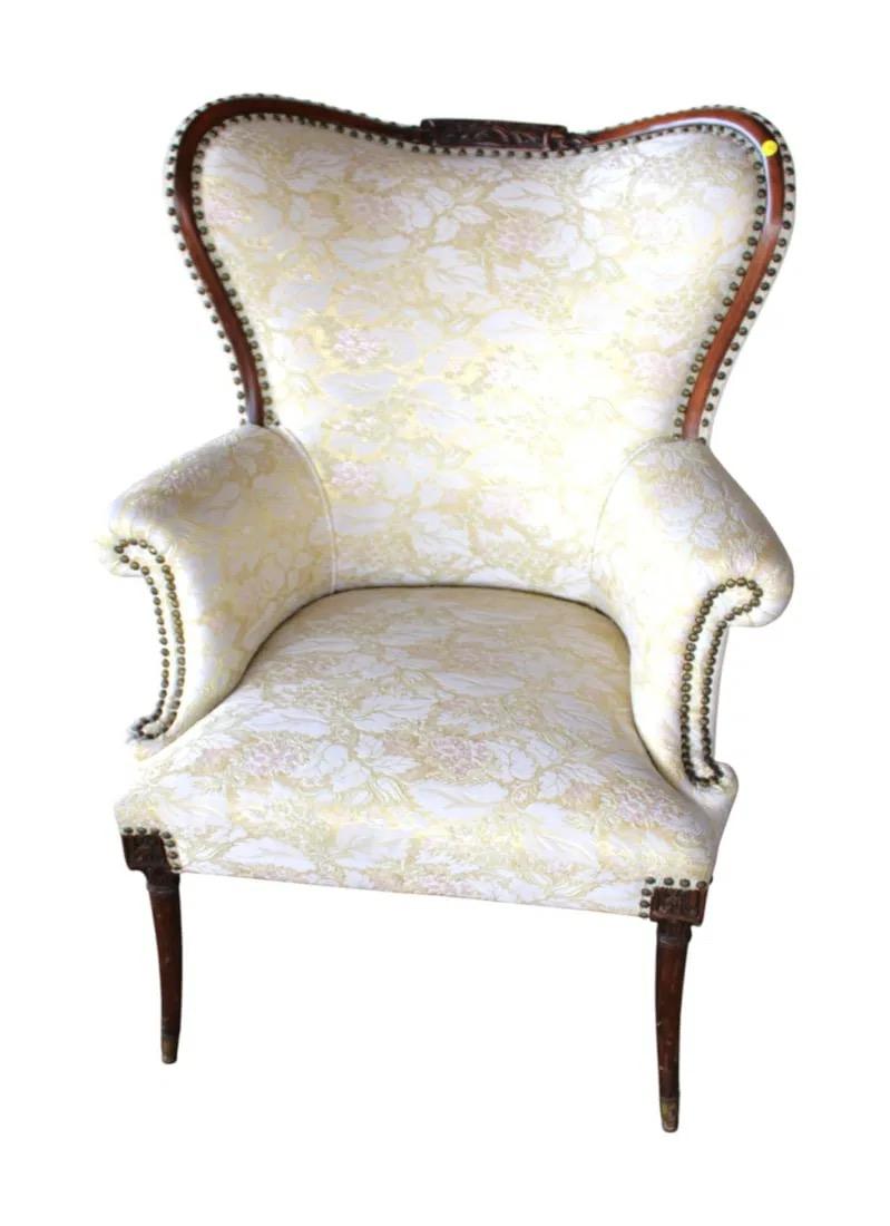 Mahogany-framed wingback chair with carved crest, rolled arms, and brass nailhead trim. Upholstered in yellow and cream floral fabric. Tapered wooden legs. 


