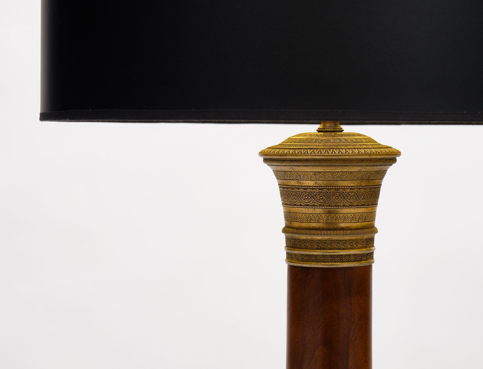 Floor lamp in the French empire style by Maison Jansen. This piece is made of mahogany with a tripod base and column leg finishing in a lustrous Museum quality French polish. The base has ebonized hand-carved claw feet. The lamp is adorned with