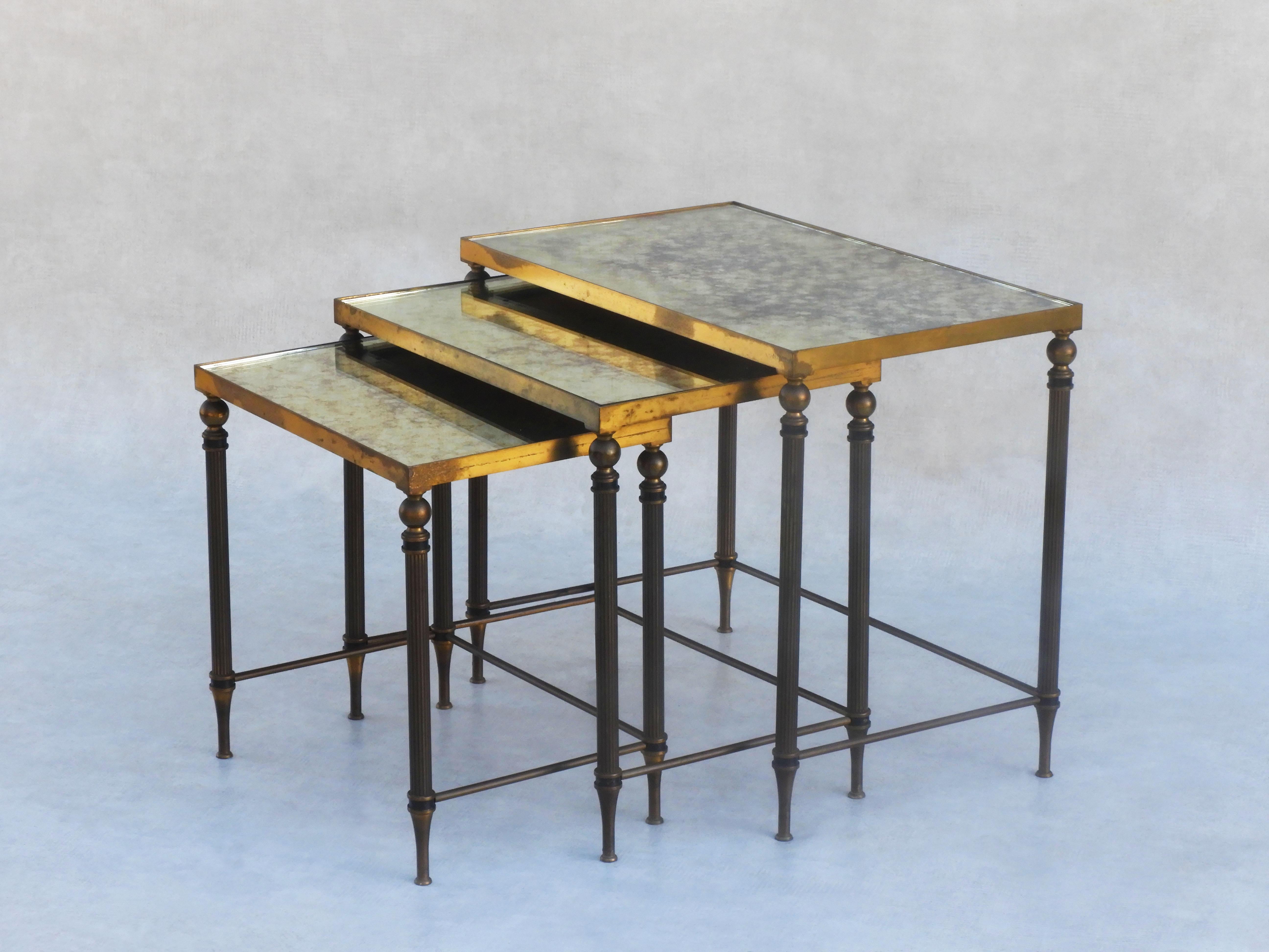 A fabulous set of mid-century nesting tables inset with 'verre églomisé' mirrored tops. Three vintage, neo-classical style tables with fluted legs and dappled gold and silver mirrored glass, in the style of French design houses like Maison Jansen,