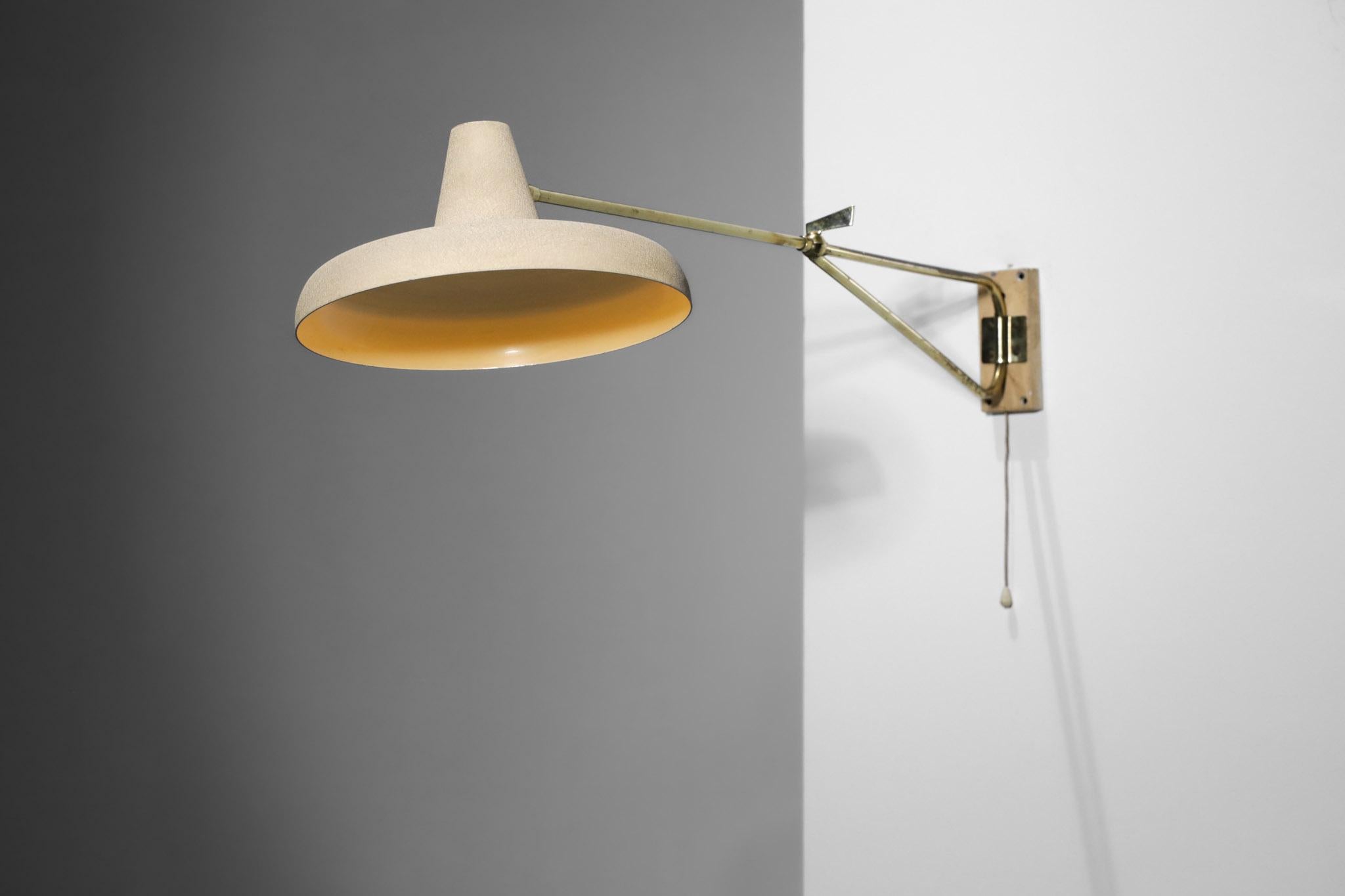 Articulated wall lamp from the 50's in the style of Lunel's work. Articulated arm in solid brass allowing to orientate the lamp in different positions. Shade and wall plate in lacquered metal with original beige vermiculated paint. Very nice vintage