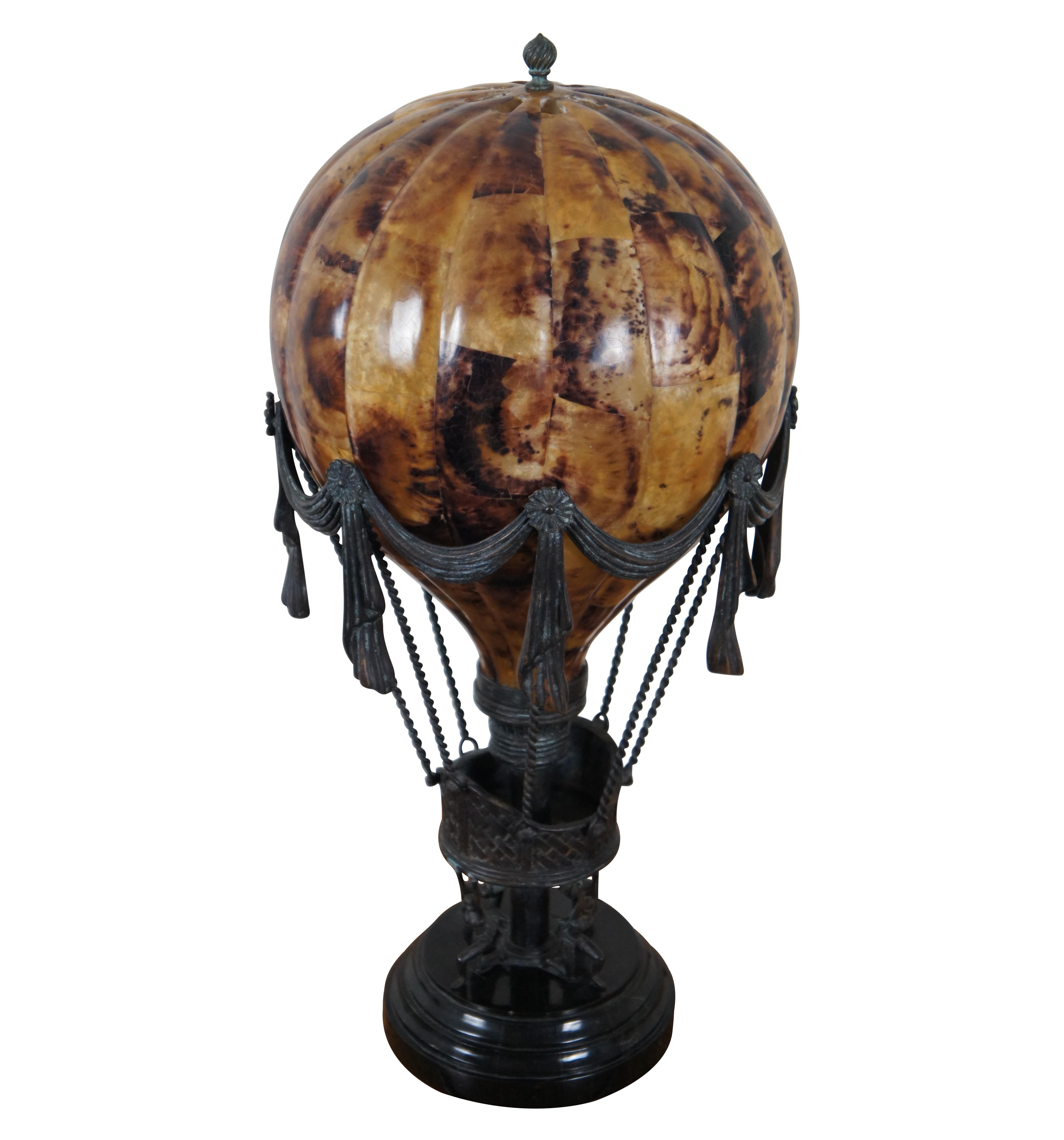 Vintage Maitland Smith table lamp with round black base supporting a bronze hot air balloon basket with taut ropes and trimmed with swags of cloth, raised by four kneeling female figures and a resin / tessellated pen shell balloon shaped shade.
