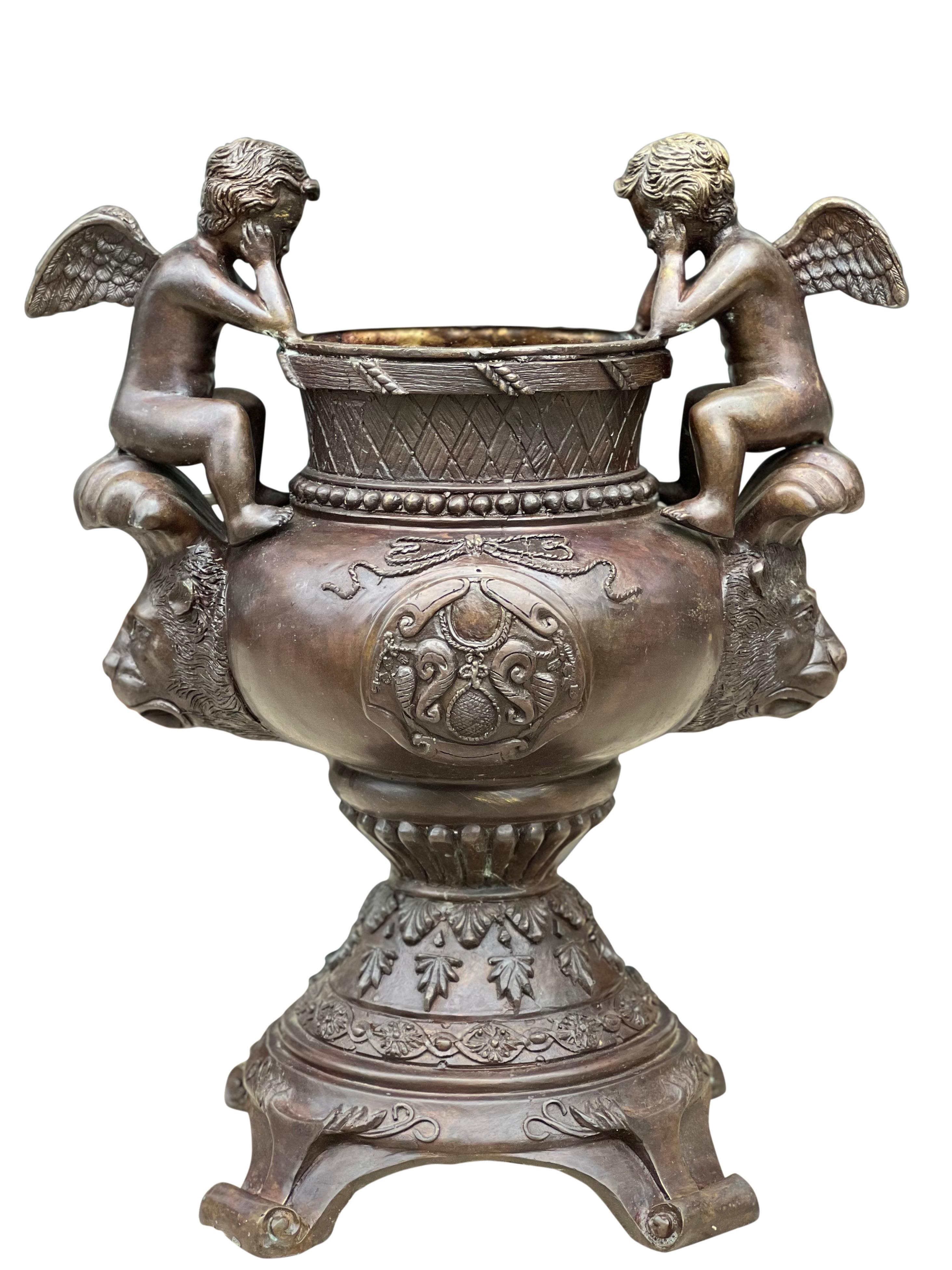Vintage Maitland Smith bronze urn with cherubs, 1980's.

This beautiful urn is flanked by seated cherubs and features lion masqueron handles. Unique footed base. Center medallion is garnished with garland and the urn is ornately detailed with