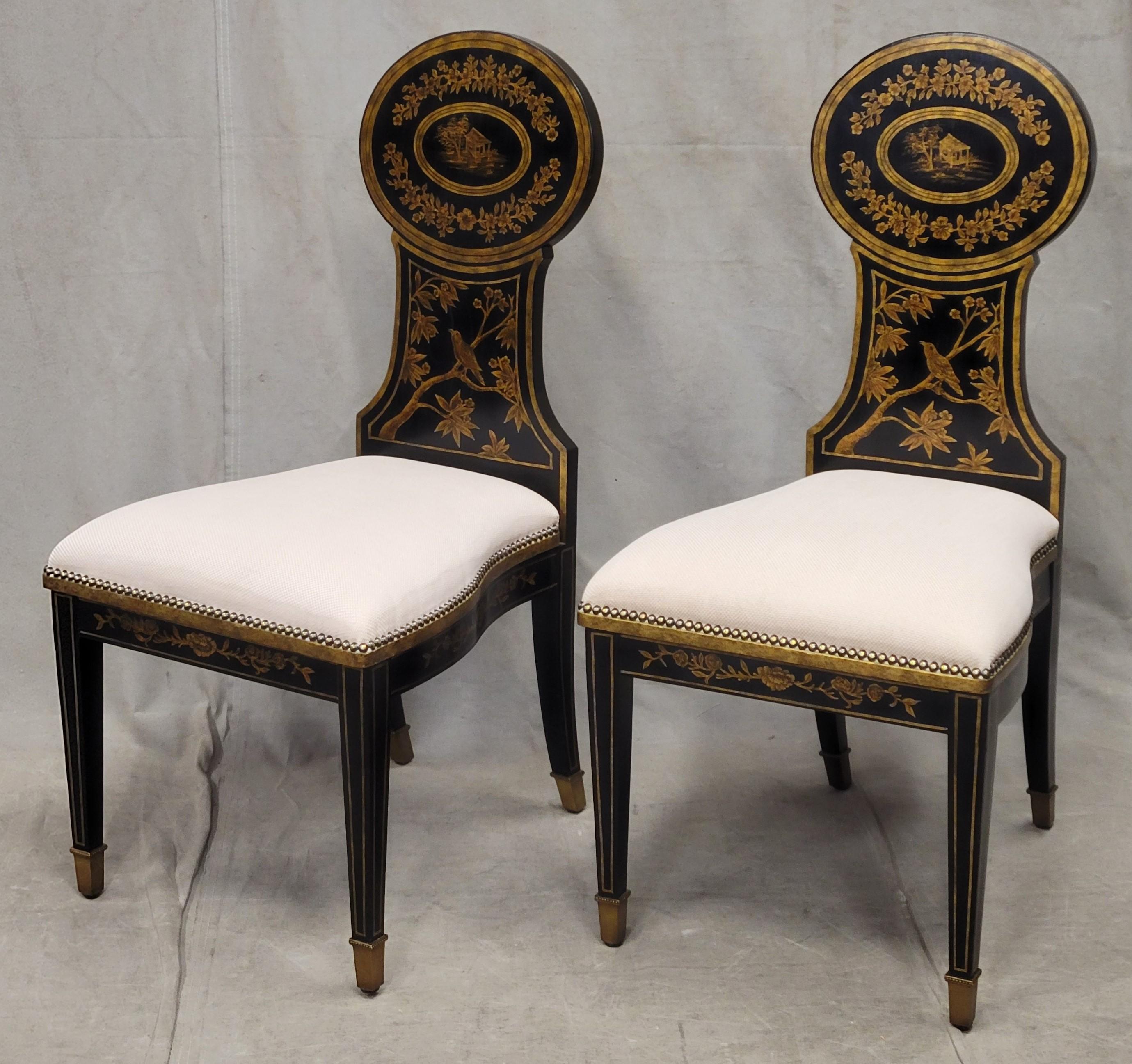 A gorgeous pair of vintage likely 1990s Maitland-Smith chinoiserie side / accent chairs in ebonized wood with gold painted accents of flowers, birds and Asian Style houses. The polished brass tacks and brass feet are shiny and gorgeous. The woven