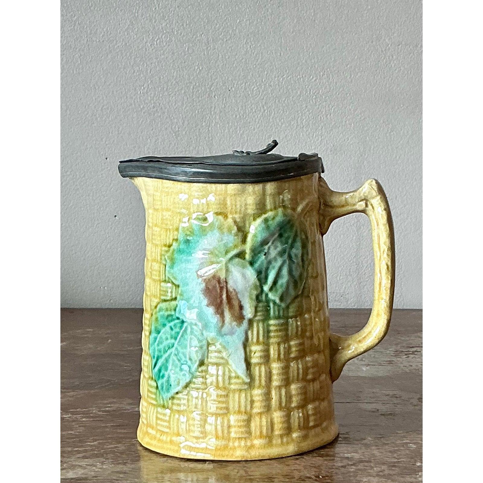 A delightful and highly collectible piece of Victorian ceramic art, this antique majolica syrup pitcher is brimming with English country charm. The body of the pitcher is masterfully molded with a classic basketweave texture and finished in a