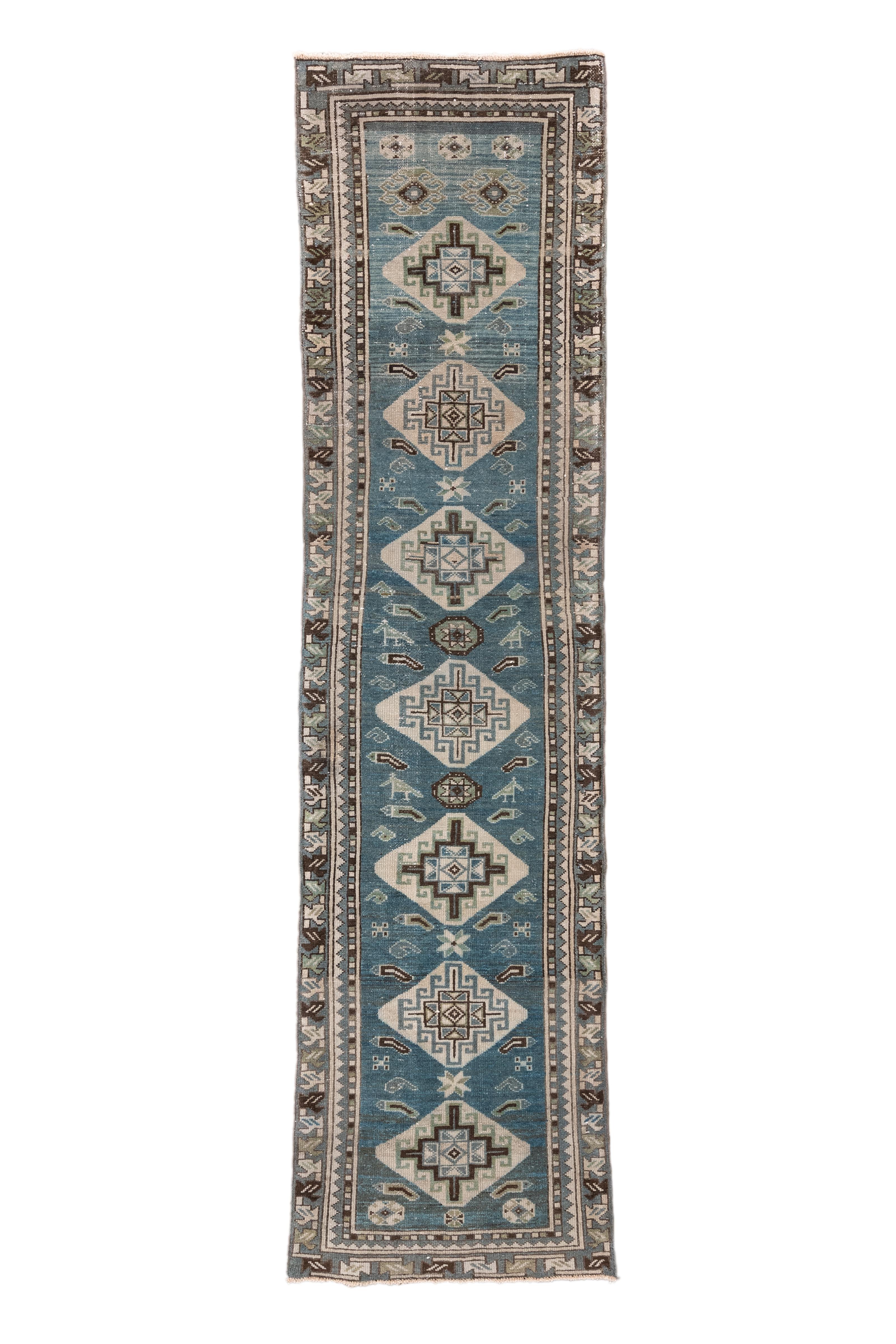 Esta alfombra Malayer de época, tejida hacia 1920, presenta una elegante serie de estilizados medallones en forma de gancho flotando sobre un luminoso campo azul celeste. Los motivos geométricos en marfil, marrón y verde azulado intenso ofrecen un