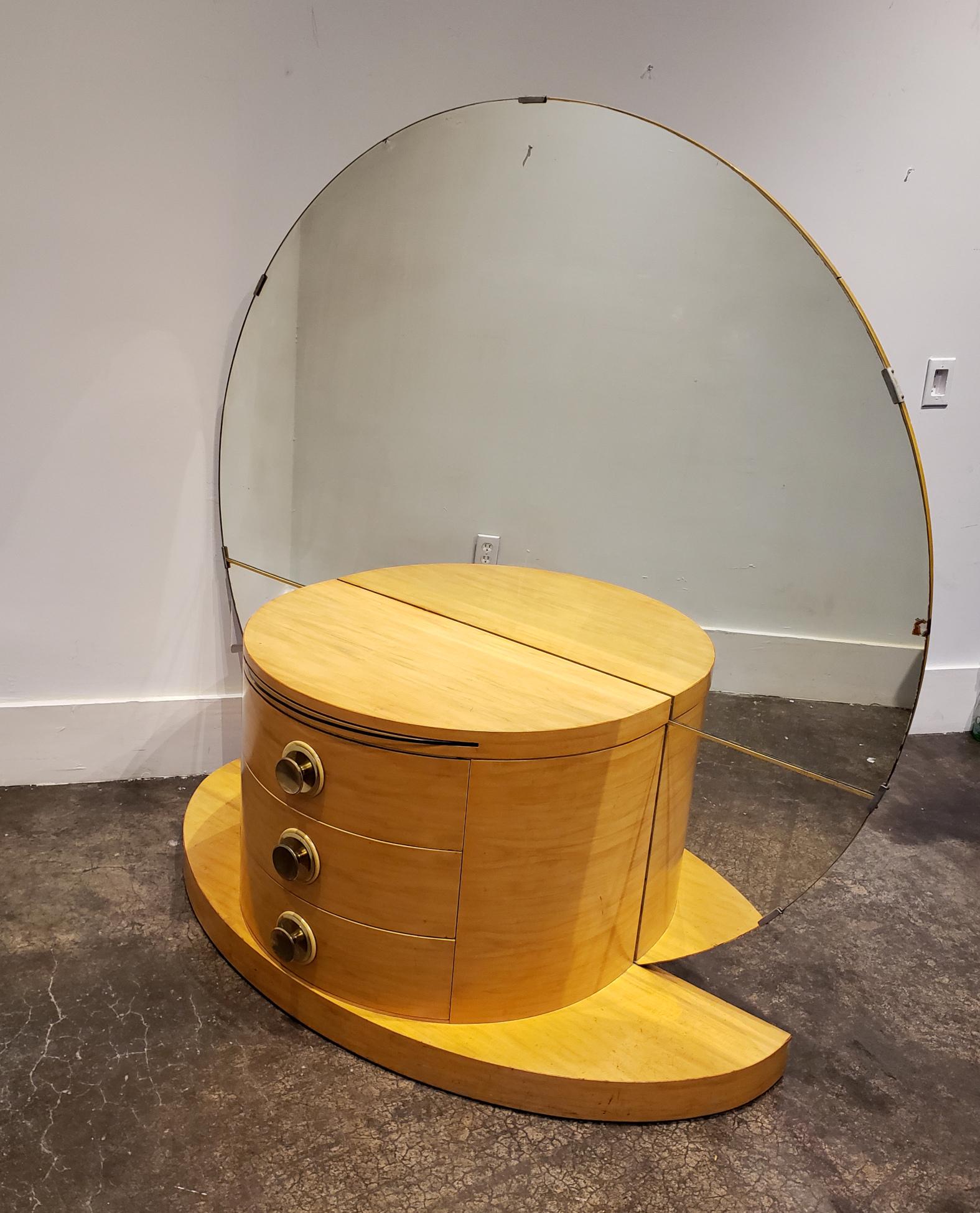 Semi-circular vanity in light maple wood veneer raised on demilune plinth. Has 3 curved drawers with metallic circular pulls and a pull-out glass shelf. Massive 61