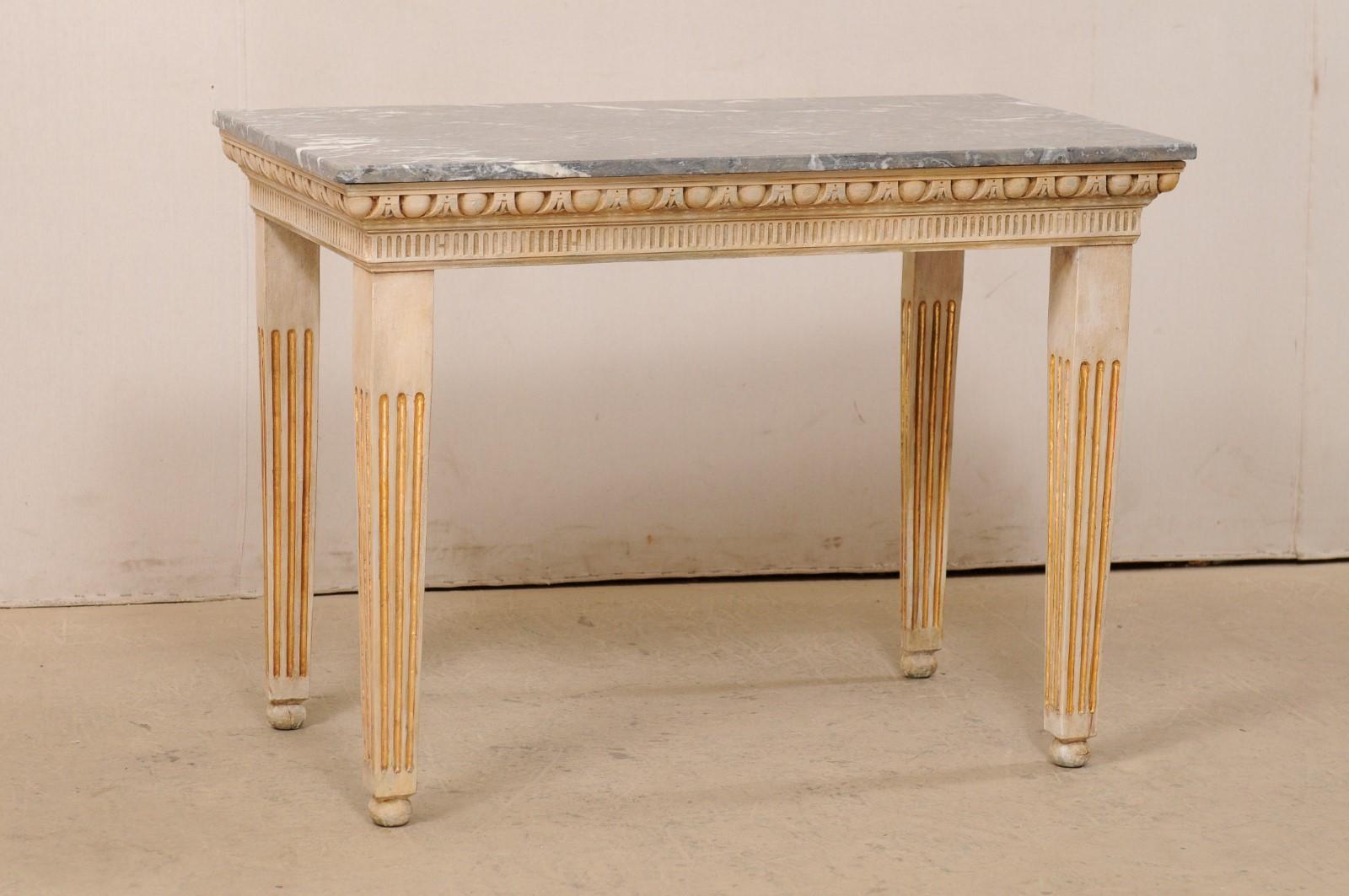 An Italian-style wood-carved console table with marble top. This vintage American table has been designed in an Italian style, featuring a rectangular-shaped marble top which rests upon a carved apron in egg-and-dart trim at top, with fluted trim at