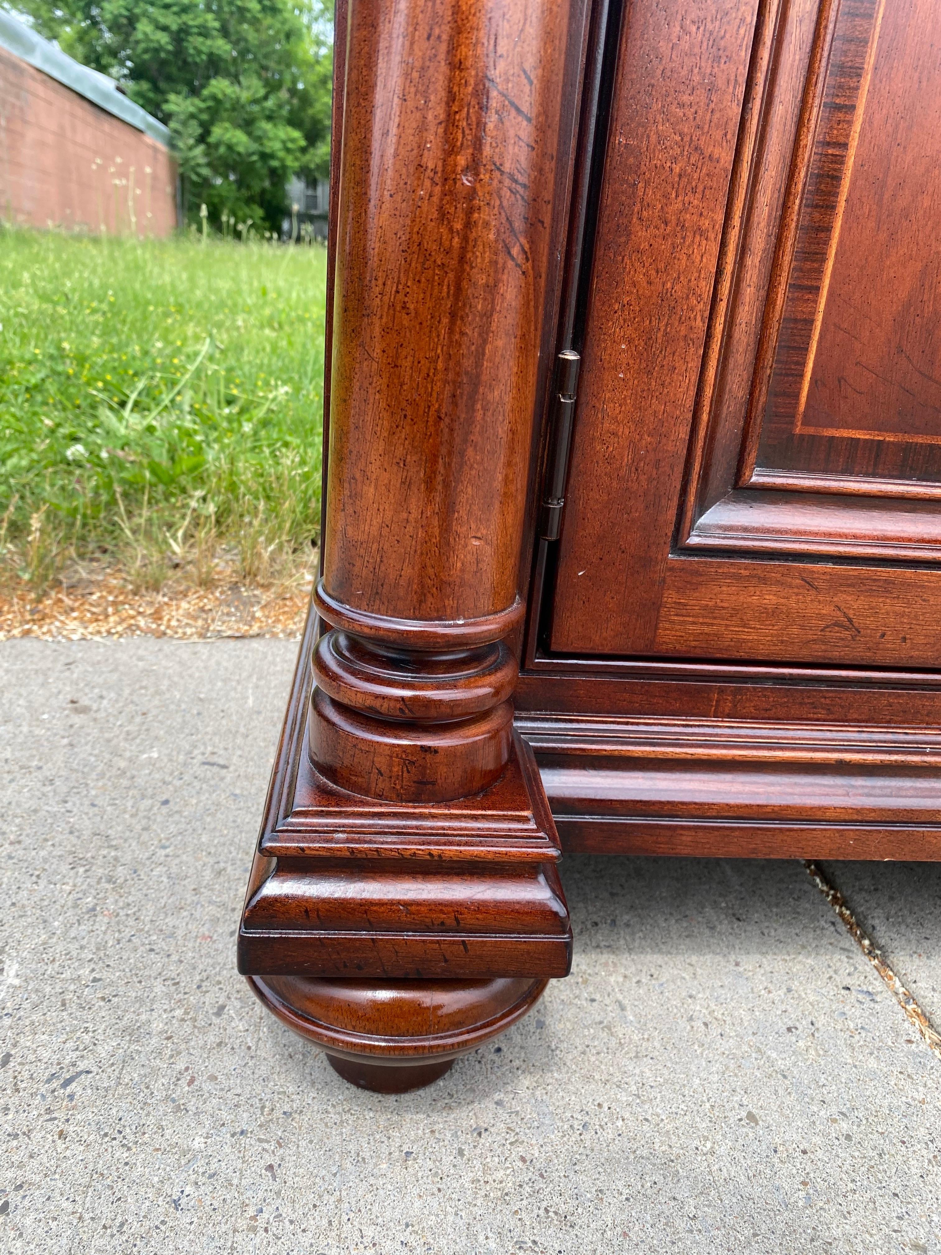 This is a handsome four-door marble topped credenza by Thomasville. This credenza features a brown marble top with cream colored veining. This credenza has drawers at the top and four doors at the bottom. The credenza has four columns and stands on