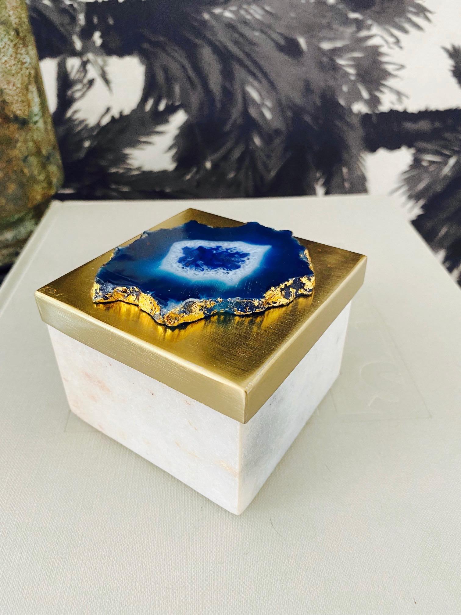 Handcrafted trinket box in white polished marble. The box has a brass lid with a brushed satin finish and is fitted with an agate stone inset. The stone has hues of lapis blue, turquoise, and white with gold plated edges. Makes a chic accent to any