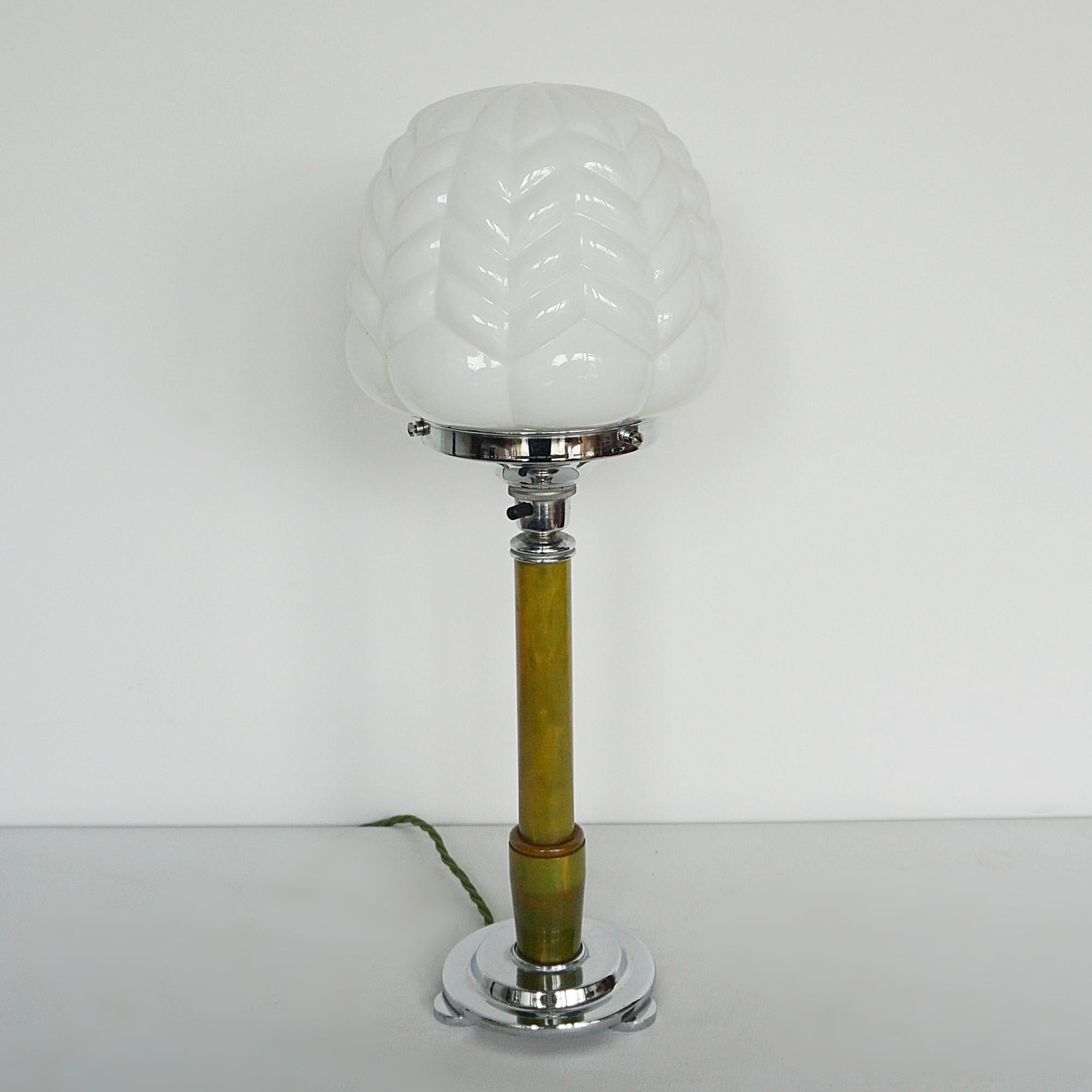 Lámpara de mesa Art Decó. Vástago de baquelita verde jaspeado con base circular de metal cromado y pantalla blanca esmerilada,
Toda nuestra iluminación está totalmente renovada, recableada y recromada con algunas piezas de repuesto.
