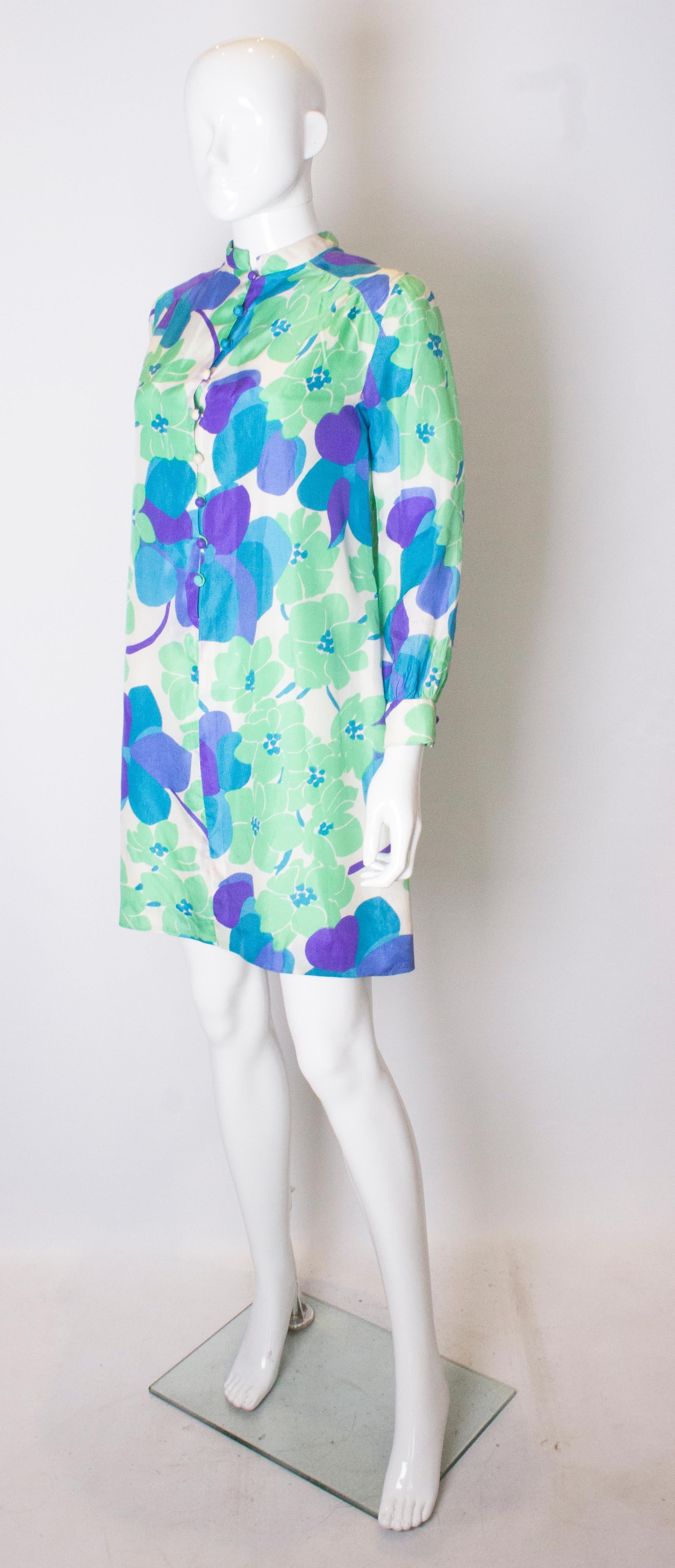 A colourful vintage silk shirt /tunic by Marcel Fenez.  The shirt is in a bright print of green, purple and blue. It has a 2 button cuff, 9 button front opening and small stand up collar. It is fully lined.
