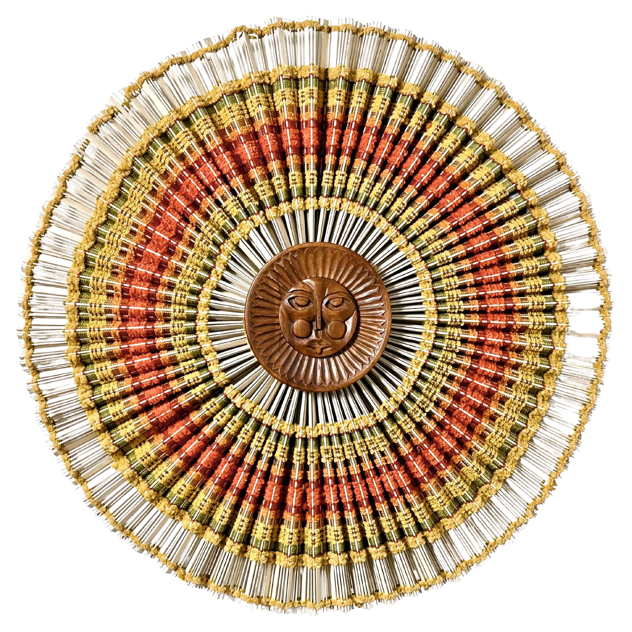 Woven fiber art wall sculpture by Maria Kipp c1960s
Dramatic sunburst of multi colored woven textiles over pleated wooden slats with a carved wood sun face center.
30 in diameter