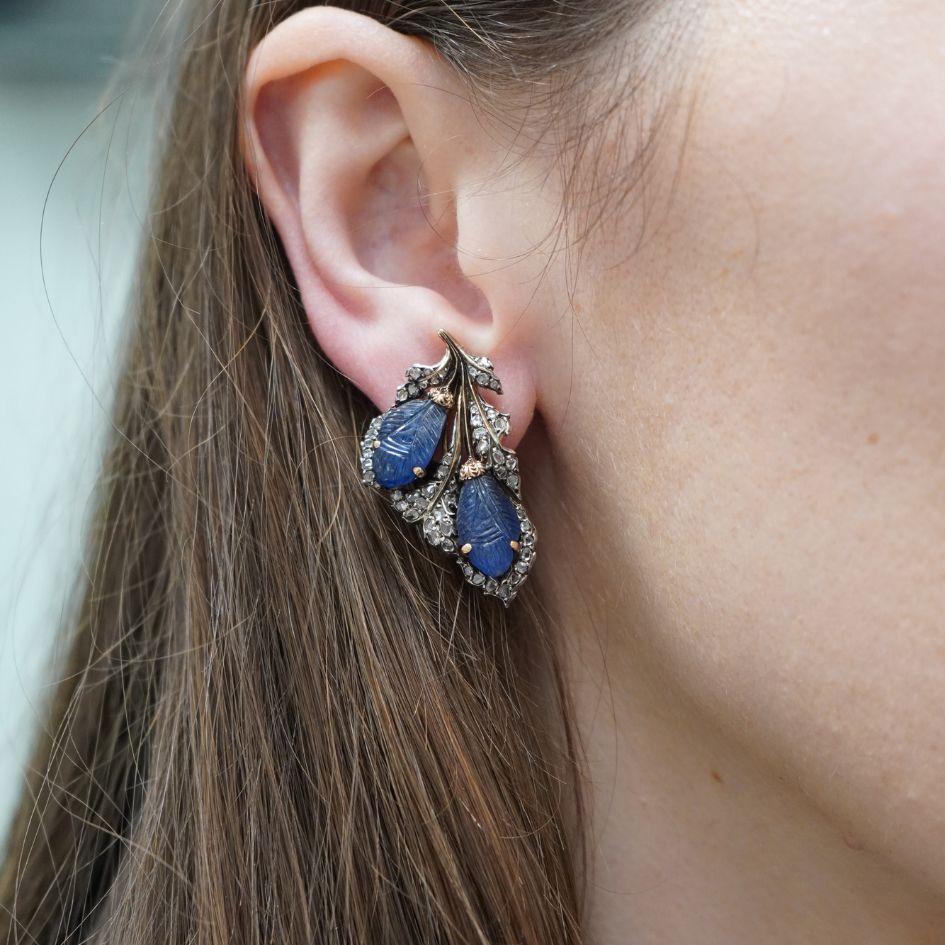 This vintage pair of clip-on earrings by Mario Buccellati showcases the house's renowned craftsmanship in mixed metals. Crafted in 18k yellow gold and silver, the earrings feature carved blue sapphire leaves accented by rose cut diamonds. The