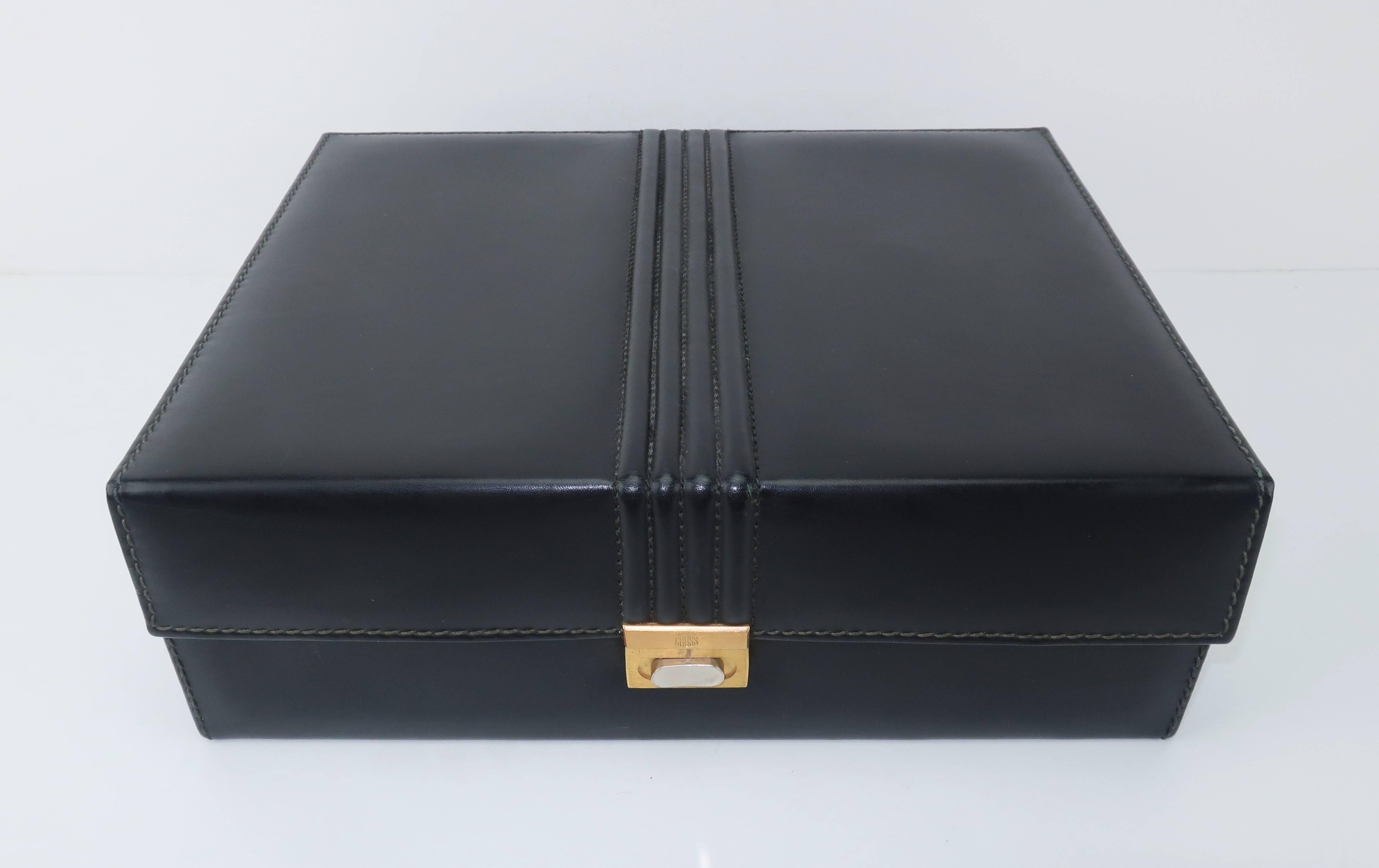 This handsome Mark Cross jewelry box is suitable for a man or woman and is practical for storage in a drawer or on a shelf.  The black leather case is channeled across the top with a fold over front which features a brushed metal push button