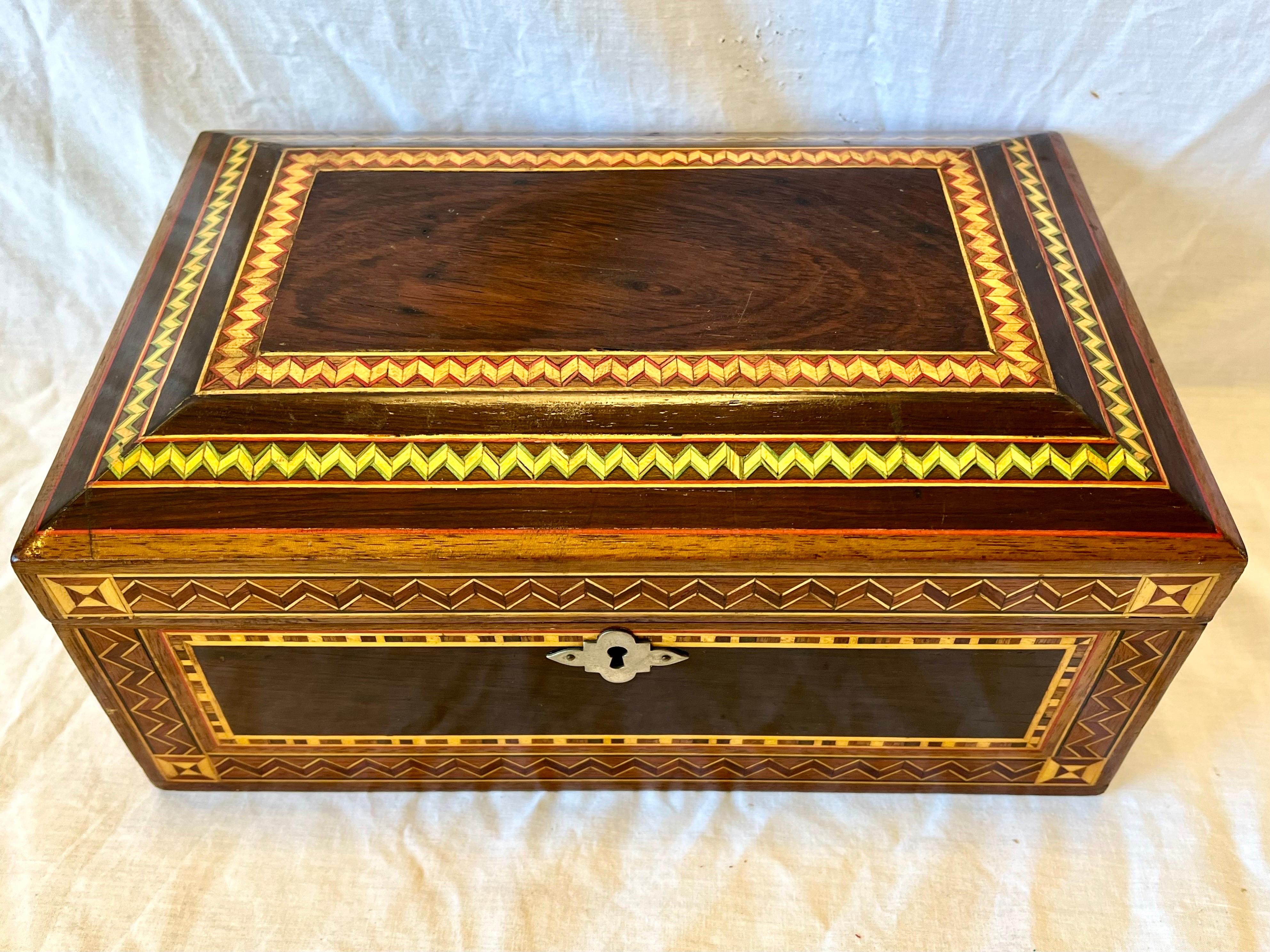 A beautiful vintage marquetry inlaid jewelry casket or box with a red velvety fabric lining the interior and an oval shaped mirror affixed to the inside of the hinged lid. The wonderfully detailed wood inlay designs are geometric in presentation.