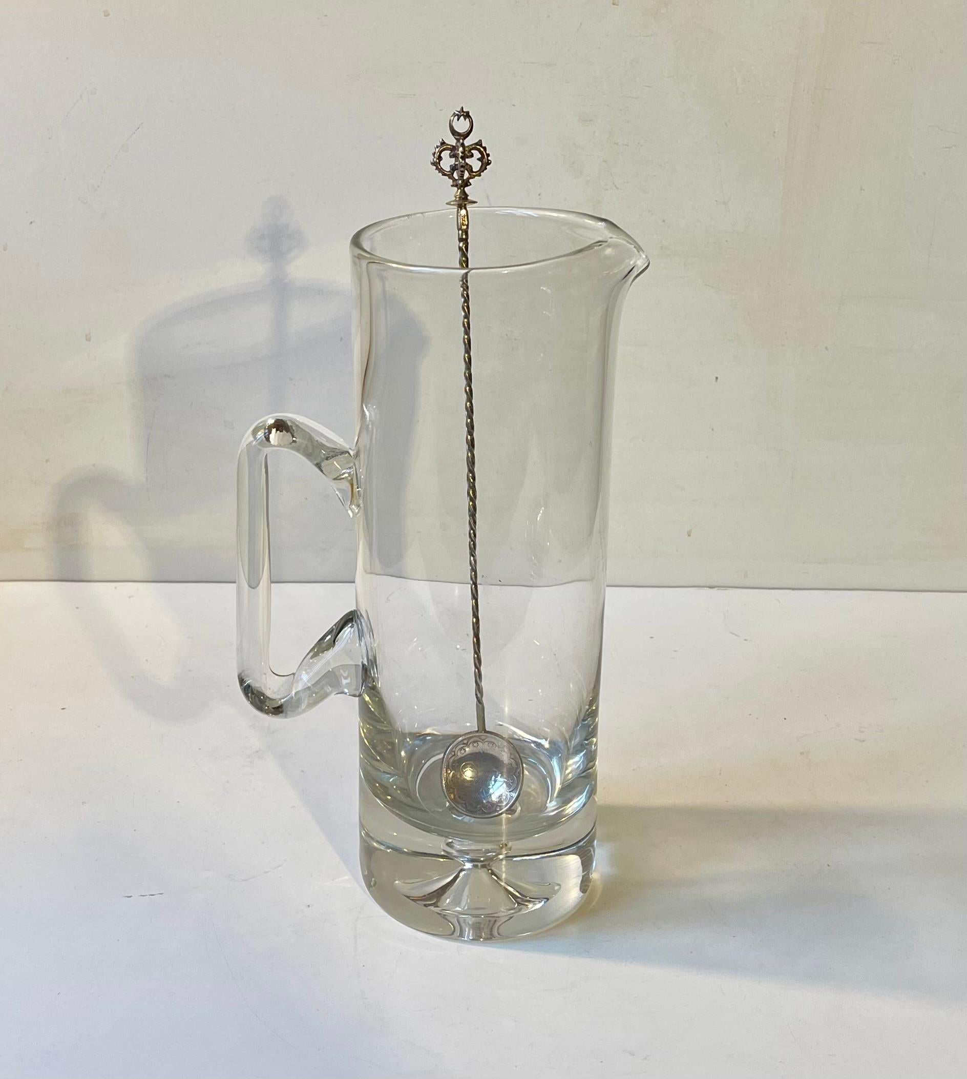 Elegante jarra soplada a mano de cristal transparente, acompañada de una batidora de Martini turca vintage de plata maciza Hallmarked 800/1000. El cabezal de la cuchara presenta una moneda de plata antigua/antigua que aún conserva sus biseles y