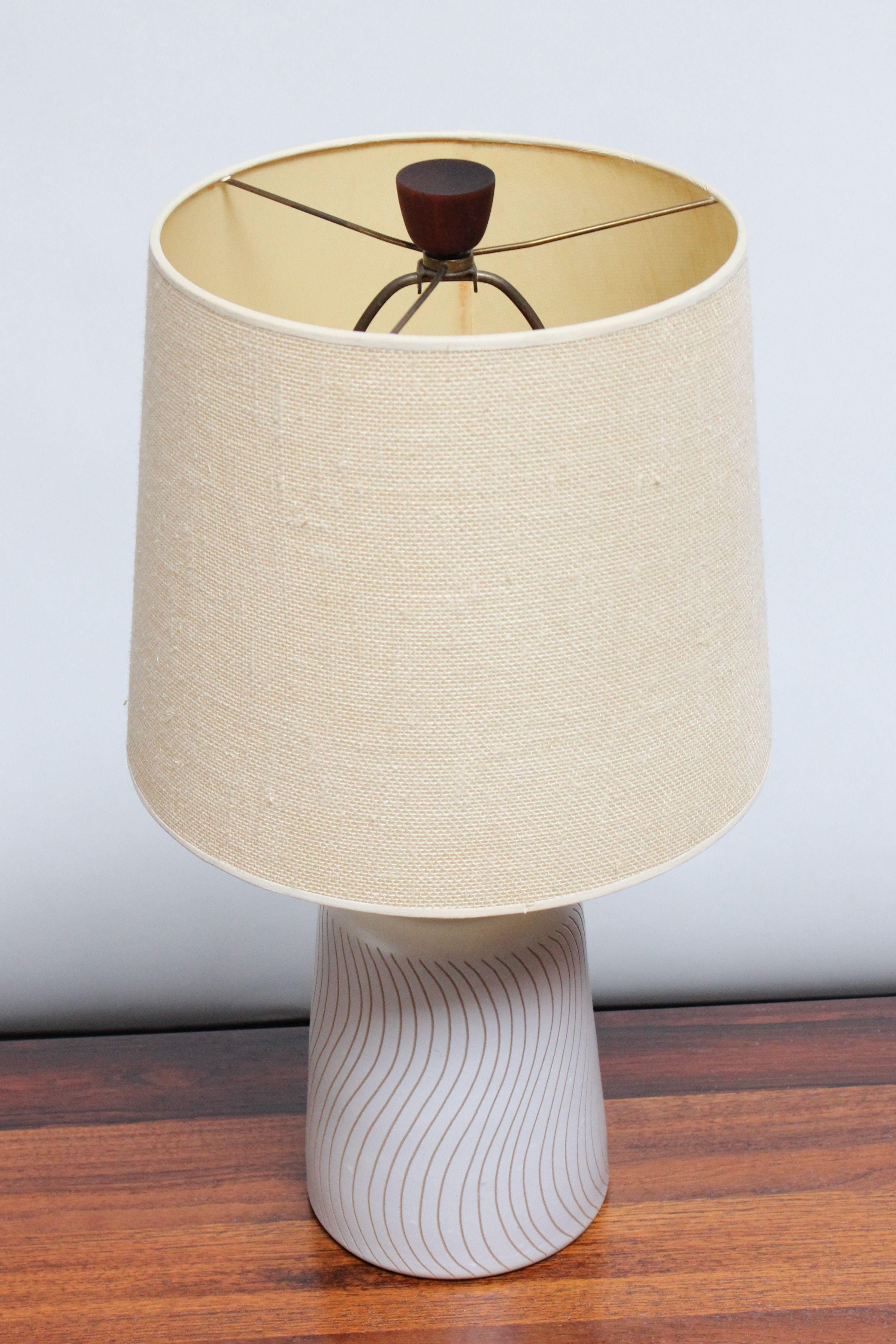 Petite Jane and Gordon Martz table lamp for Marshall Studios (ca. 1960s, USA). Features a pale gray cylindrical base with a wave Sgraffito pattern in light brown.
Nice walnut accents present in both the original final and stem.
Incised 