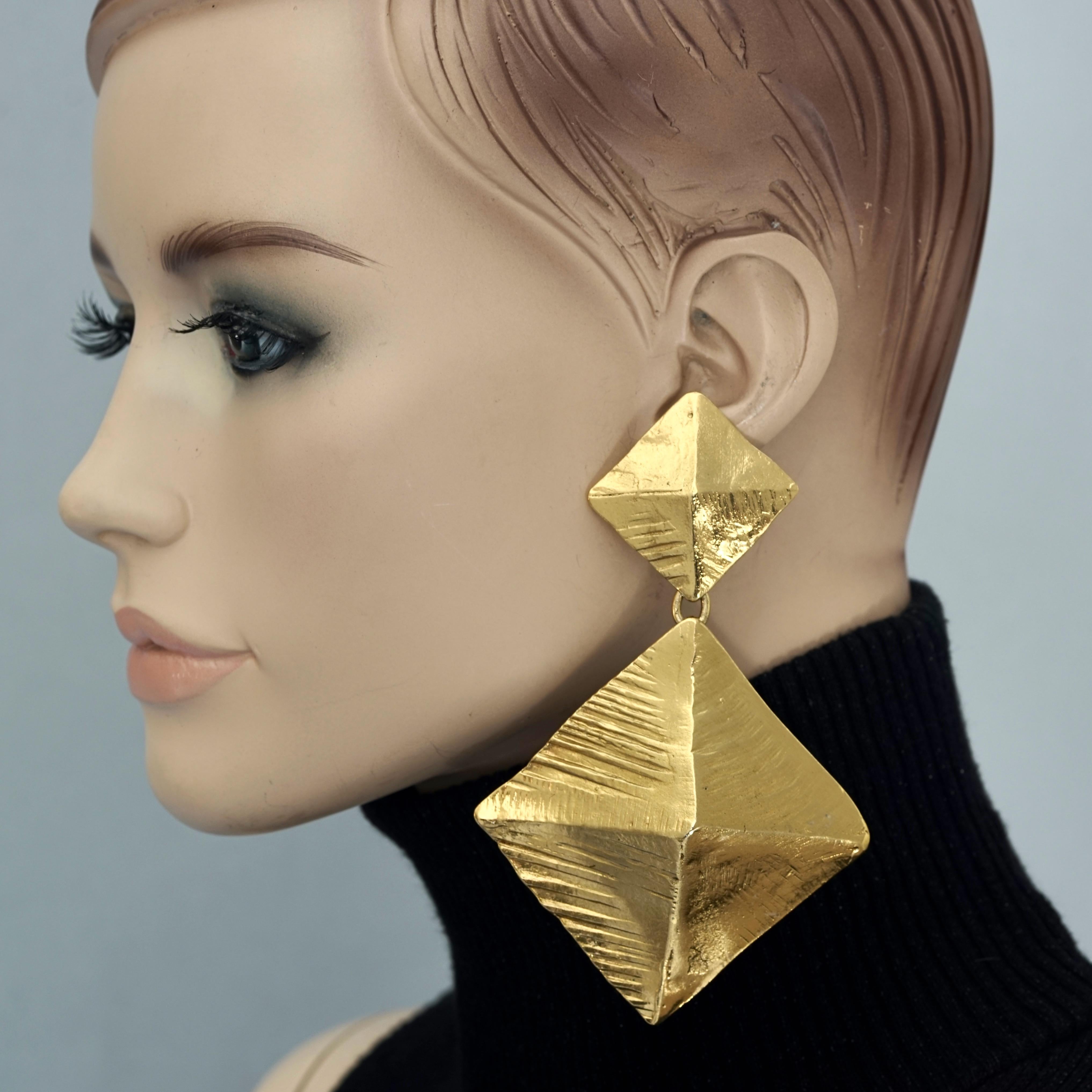 Vintage Massive YVES SAINT LAURENT Ysl Pyramid Dangling Earrings

Measurements:
Height: 4.52 inches (11.5 cm)
Width: 2.95 inches (7.5 cm)
Weight per Earring: 47 grams

Features:
- 100% Authentic YVES SAINT LAURENT.
- Massive textured double pyramid