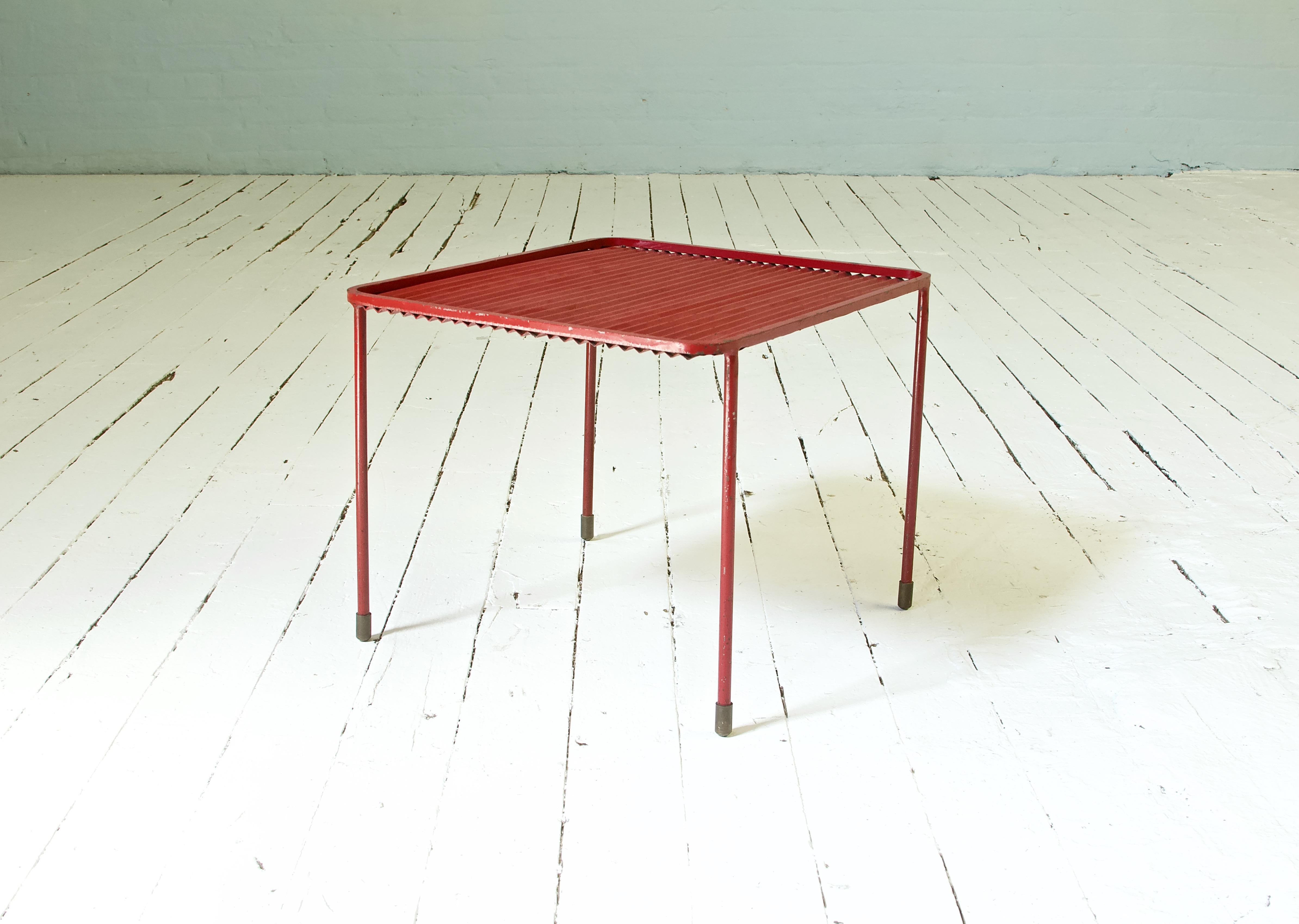 A fun little accent table in corrugated steel with brass sabots in well-preserved, bright primary red. Classic modernist usage of Industrial materials, simple lines, clean metalwork, and good proportions. This petite piece could function as an ad