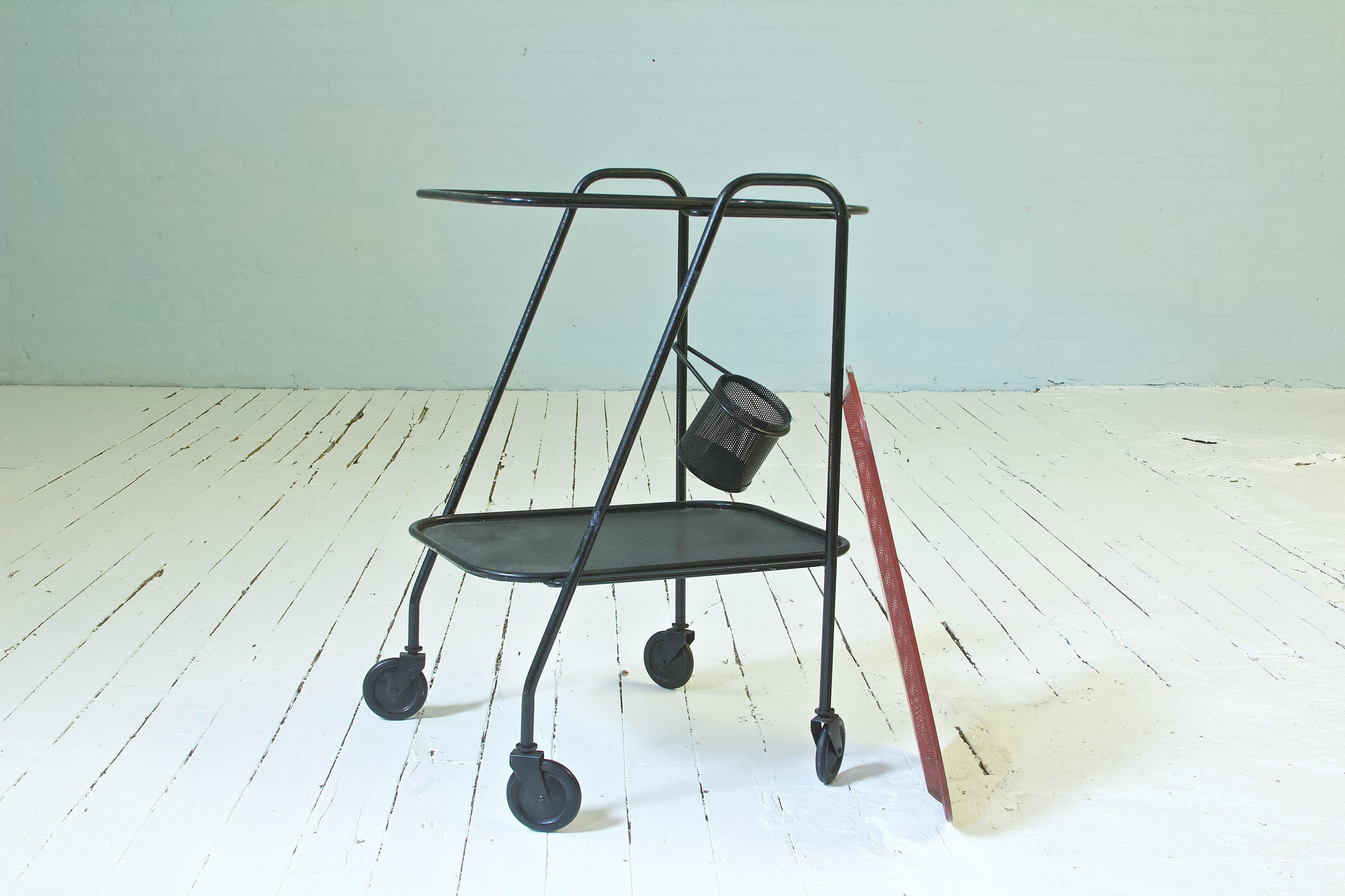 Well proportioned and useful bar cart with playful, dynamic lines and a lovely patina. The top tier of this two tiered rolling trolley, which is red-painted perforated steel, is removable to allow for direct service of one's guests. There is a