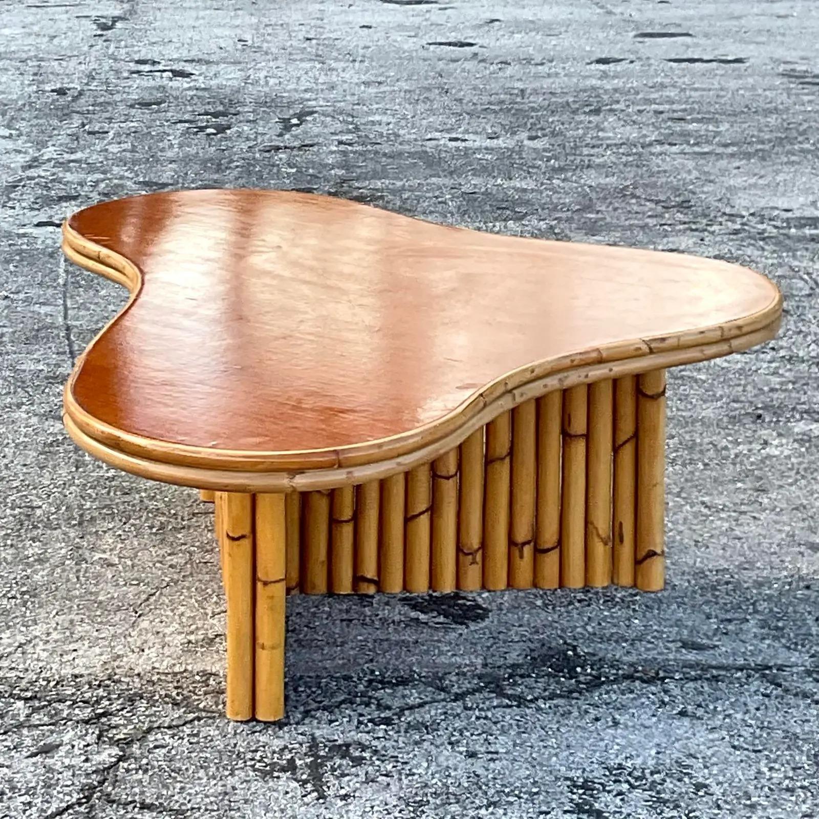 A fabulous vintage MCM rattan coffee table. Done in the manner of Paul Frankl. A chic amoeba shape with a intersectional rattan base. A mahogany top with rattan trim. Acquired from a Palm Beach estate.