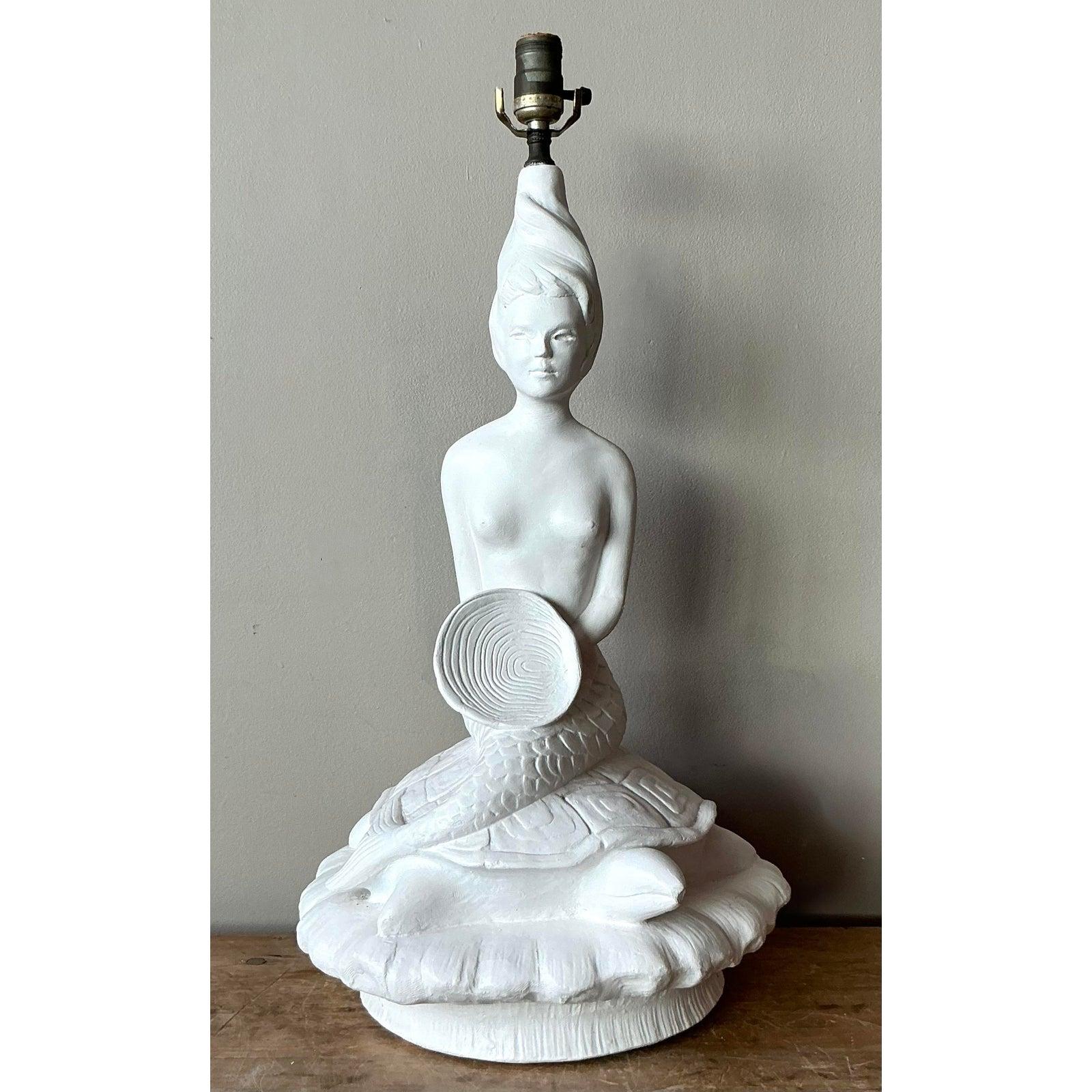 Questa accattivante lampada da tavolo vintage presenta una scultura figurativa altamente stilizzata che cattura il dramma giocoso dell'estetica Mid-Century Coastal e Hollywood Regency. La base presenta una figura di sirena seduta con un torso liscio