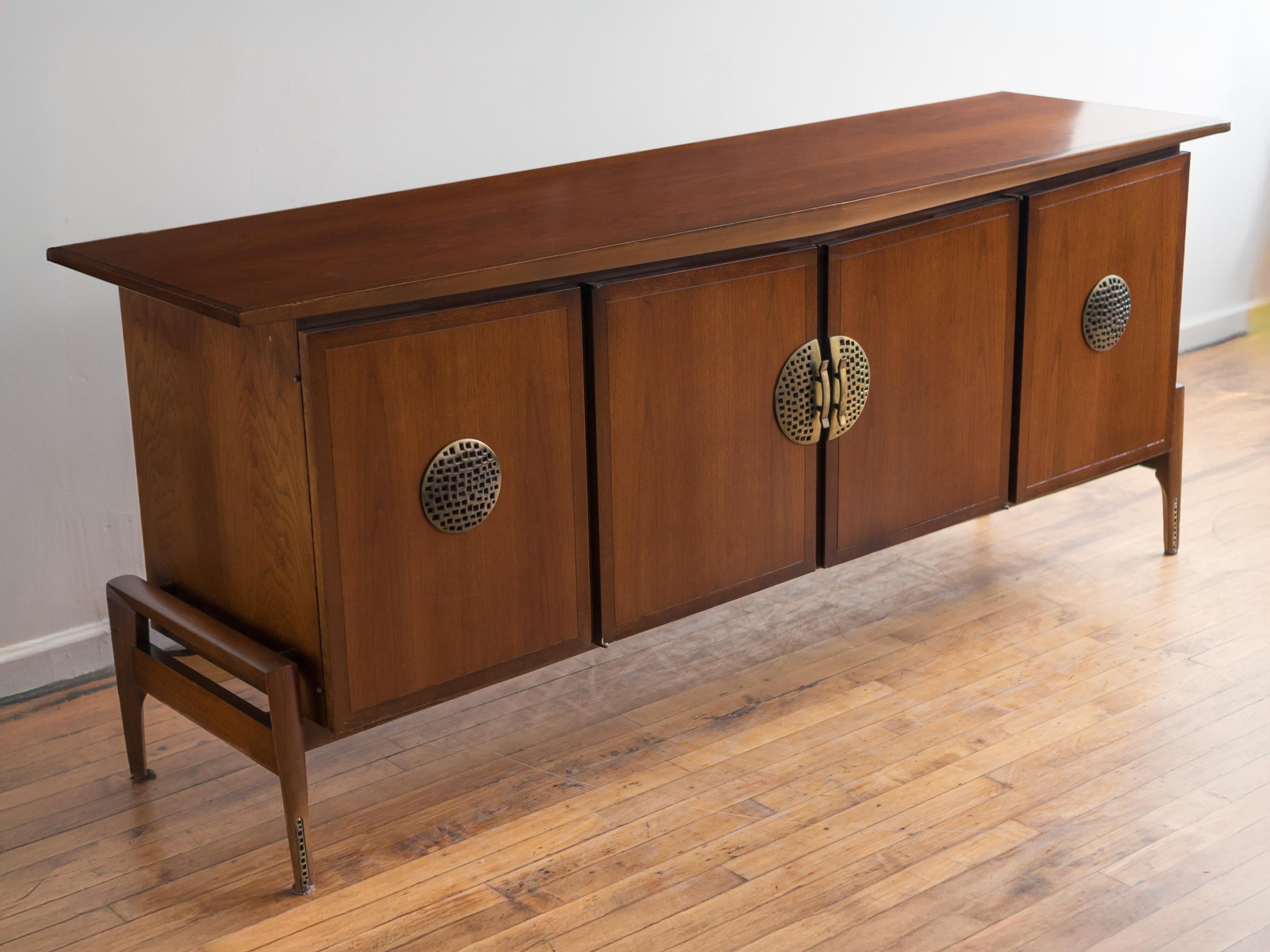 Unique mid-century credenza designed by Helen Hobey for Baker Furniture. 

• three drawers behind the left and right side doors

• open compartment with adjustable shelf behind the two middle doors

• cast metal accents on door fronts

• offset