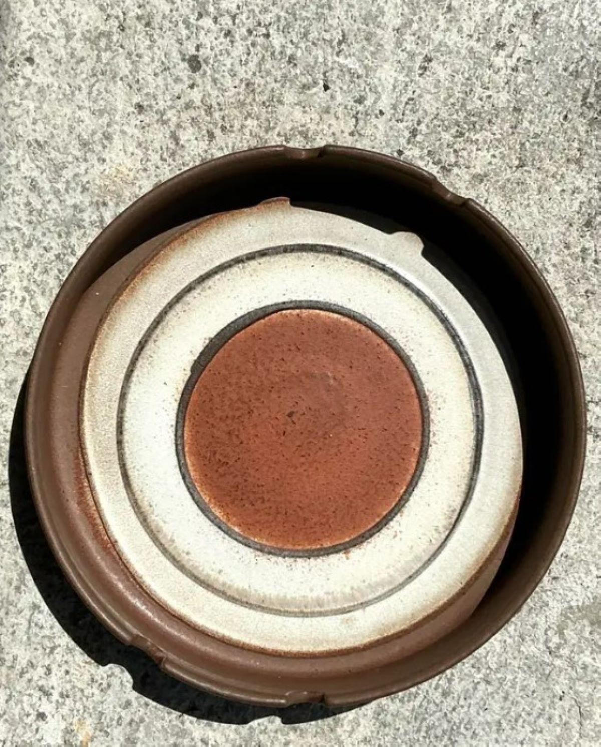 Questo posacenere vintage in ceramica della Germania Occidentale, audace e utilitaristico, incarna il classico design moderno della metà del secolo con un tocco monumentale. Realizzato in un sorprendente mix di finiture opache e smaltate, il motivo