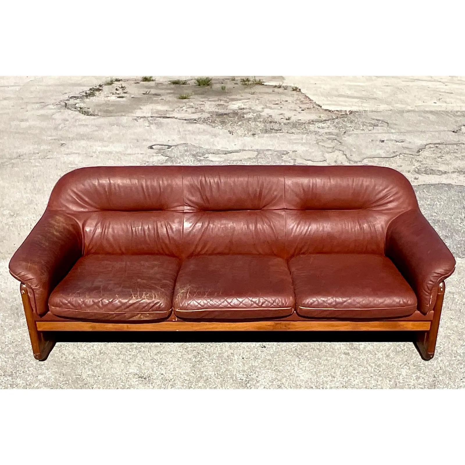 Vintage Midcentury leather sofa. Beautiful channel tufted design with a one piece cushion. Warm wood trim with inset leather panels. Acquired from a Palm Beach estate.