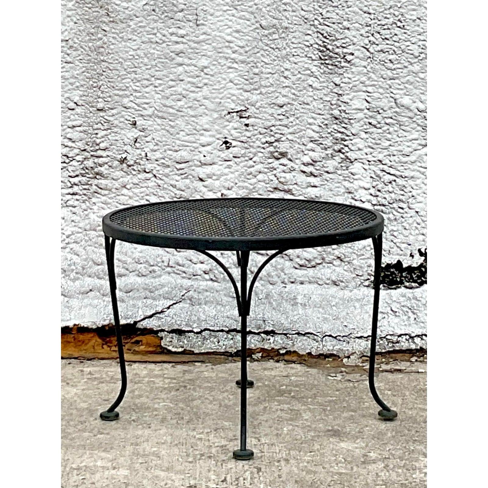 Dieser schmiedeeiserne Beistelltisch im Vintage-Stil ist eine zeitlose Anspielung auf das Outdoor-Design der Mitte des Jahrhunderts und wurde von der ikonischen Arbeit von Russell Woodard inspiriert. Die glatte, runde Netzplatte, die von eleganten,