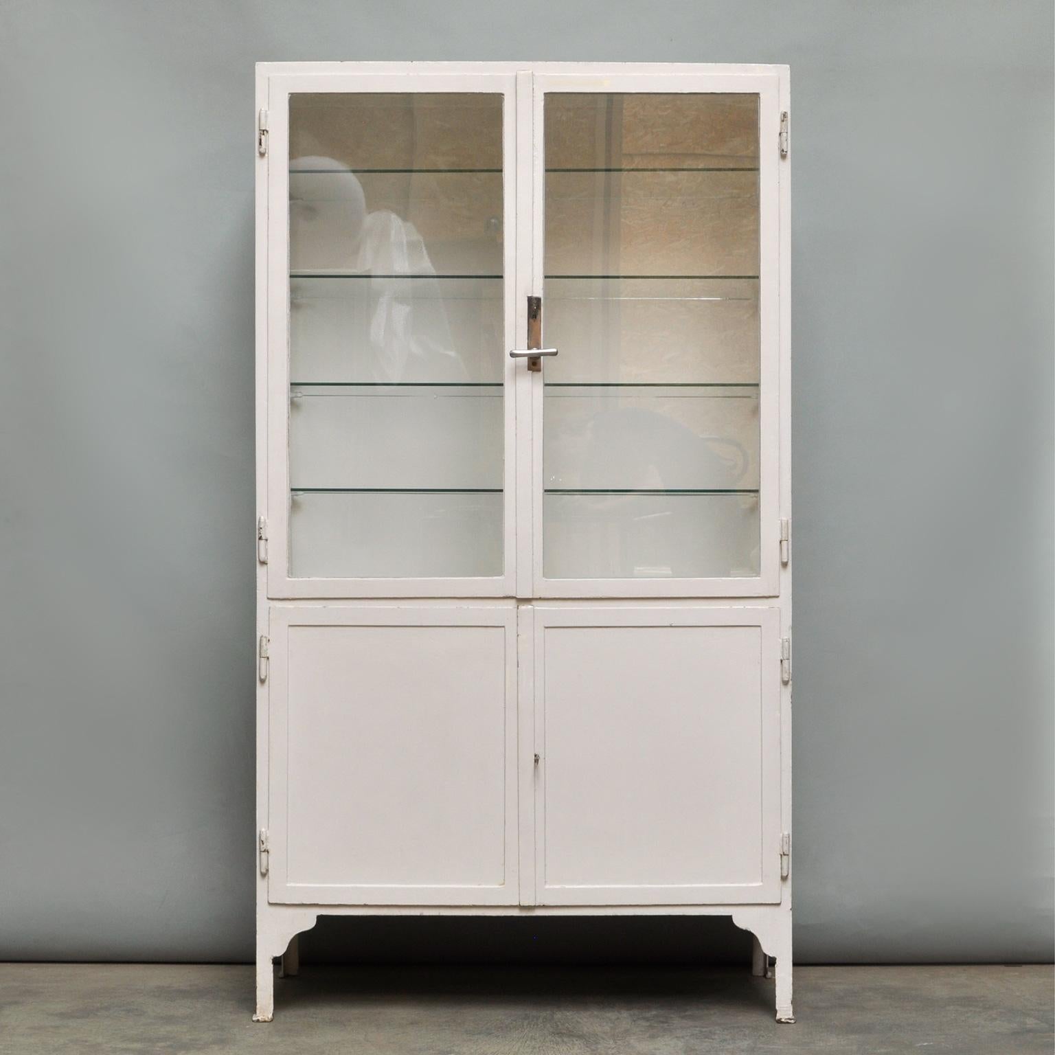 This former medical cabinet was produced in the 1940s in Hungary. It is made of thick iron and antique glass. In the upper part, there are four glass shelves. The original locks are in perfect working condition. In good condition.