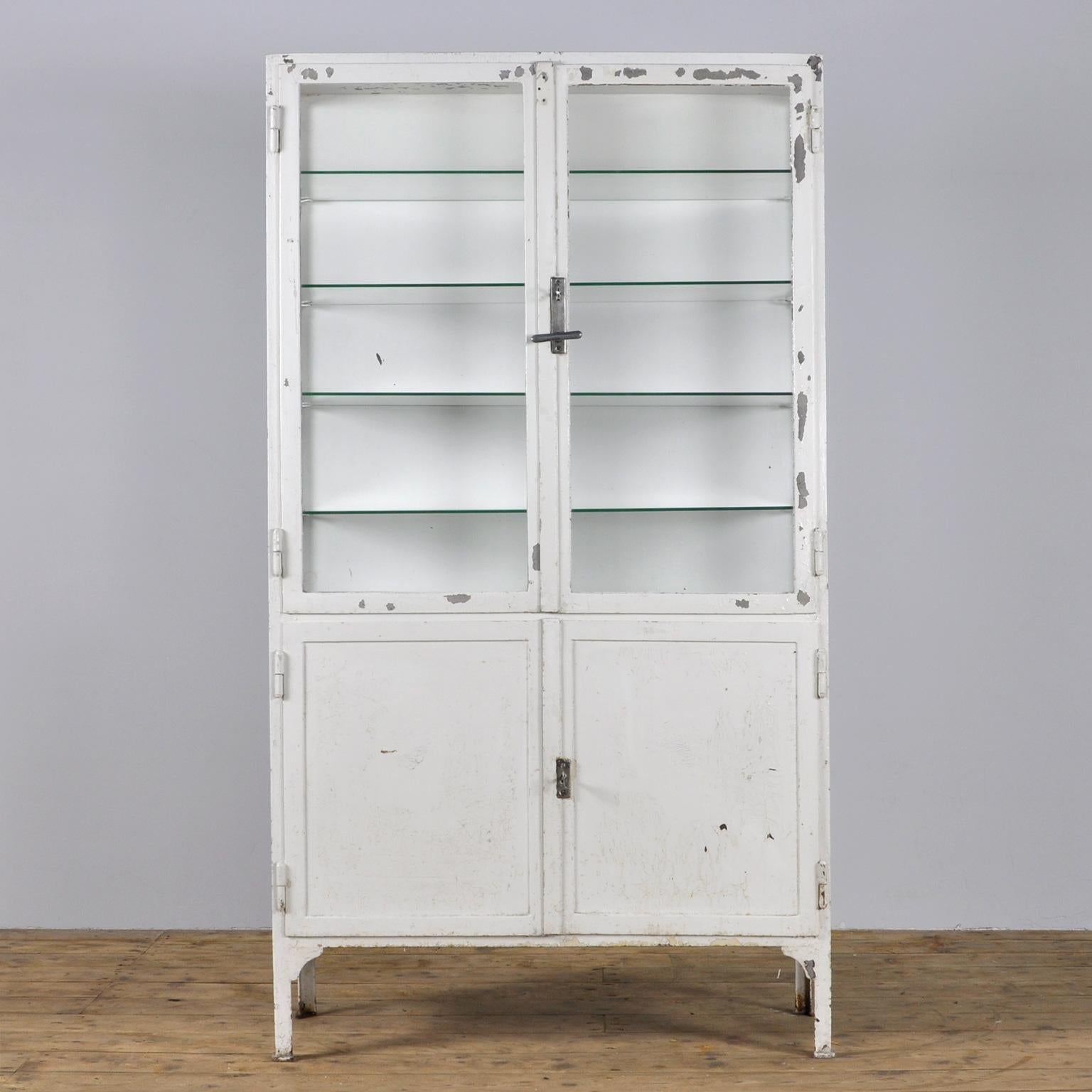 This former medical cabinet was produced in the 1940s in Hungary. It is made of thick iron and antique glass. In the upper part, there are four glass shelves. The original locks are in perfect working condition.