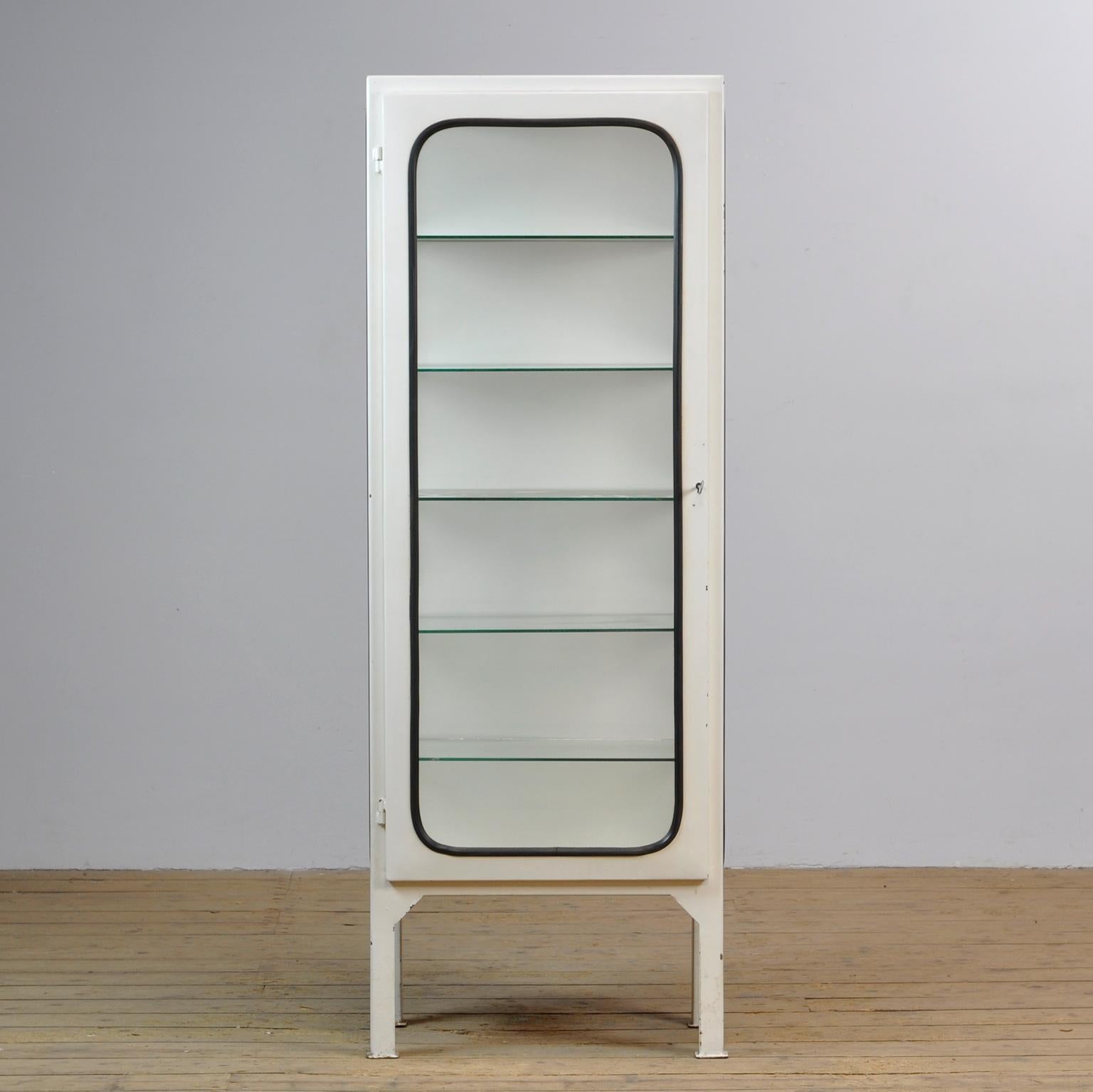 This medical cabinet was designed in the 1970s and produced in 1975 in hungary. It is made from iron and antique glass. The glass is held in place by a black rubber strip. The cabinet features five adjustable glass shelves and a functioning