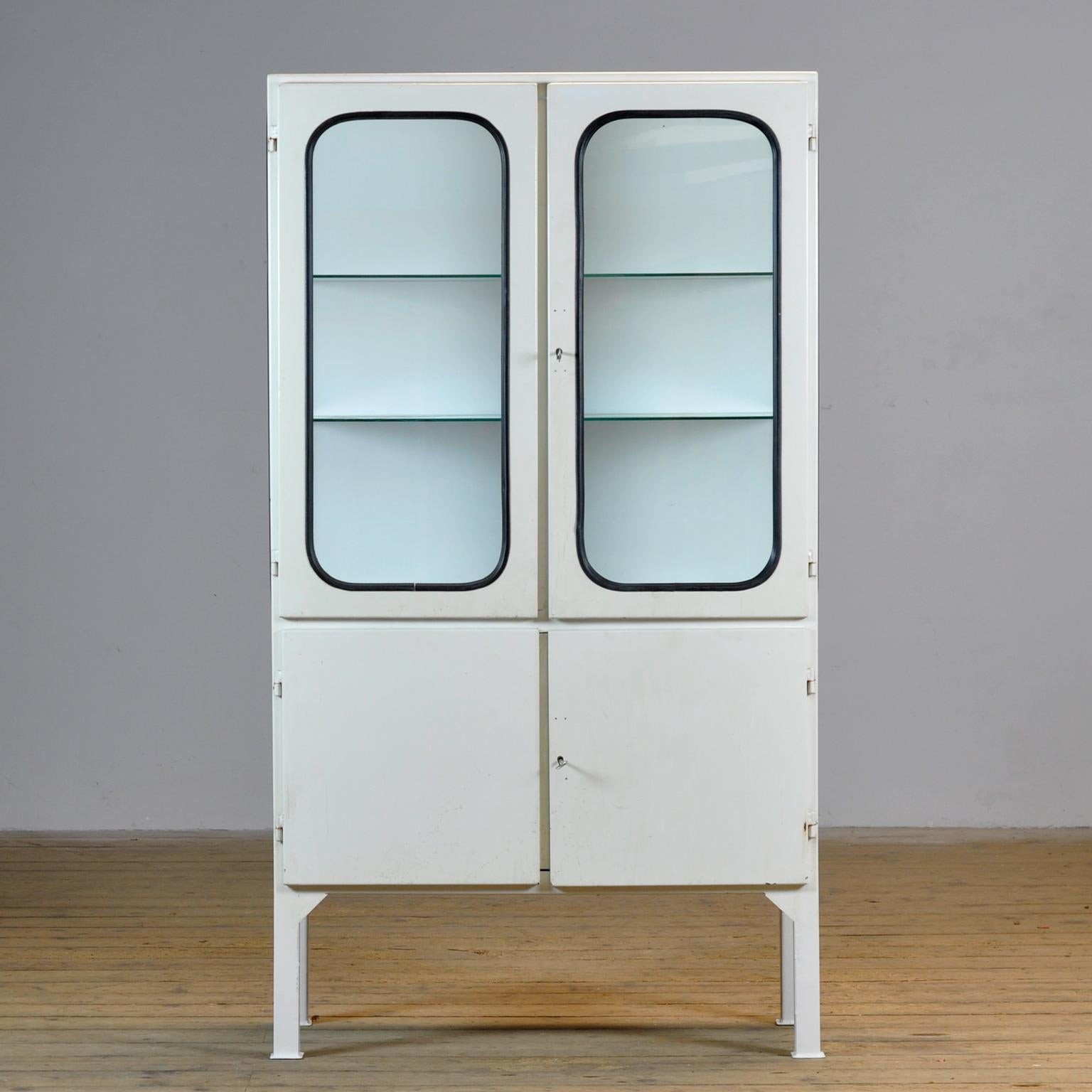 This medical cabinet was designed in the 1970s and was produced circa 1975 in hungary. It is made from iron and glass with new glass shelves. The glass is held by a black rubber strip. The cabinet features two adjustable glass shelves and