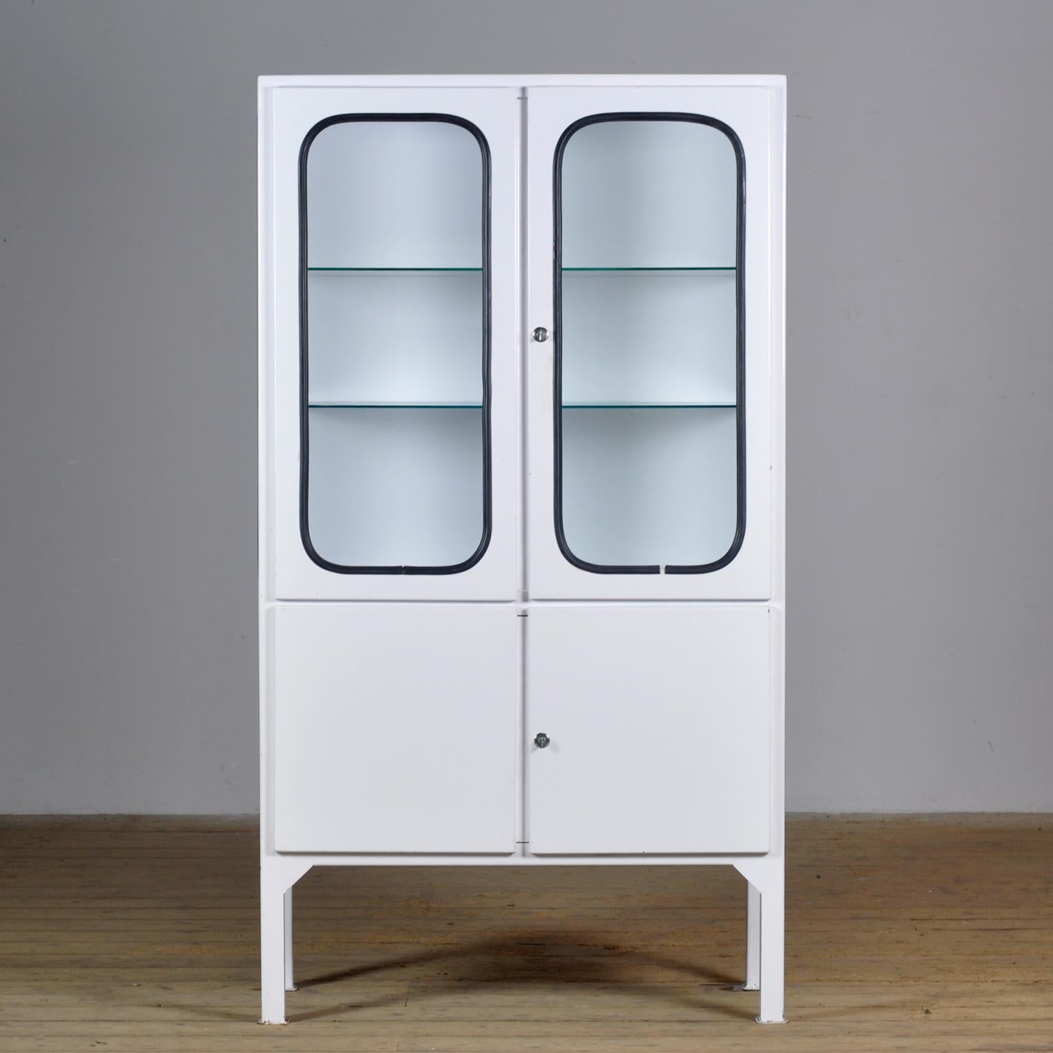 This medical cabinet was designed in the 1970s and was produced circa 1975 in hungary. It is made from iron and glass with new glass shelves. The glass is held by a black rubber strip. The cabinet features two adjustable glass shelves and