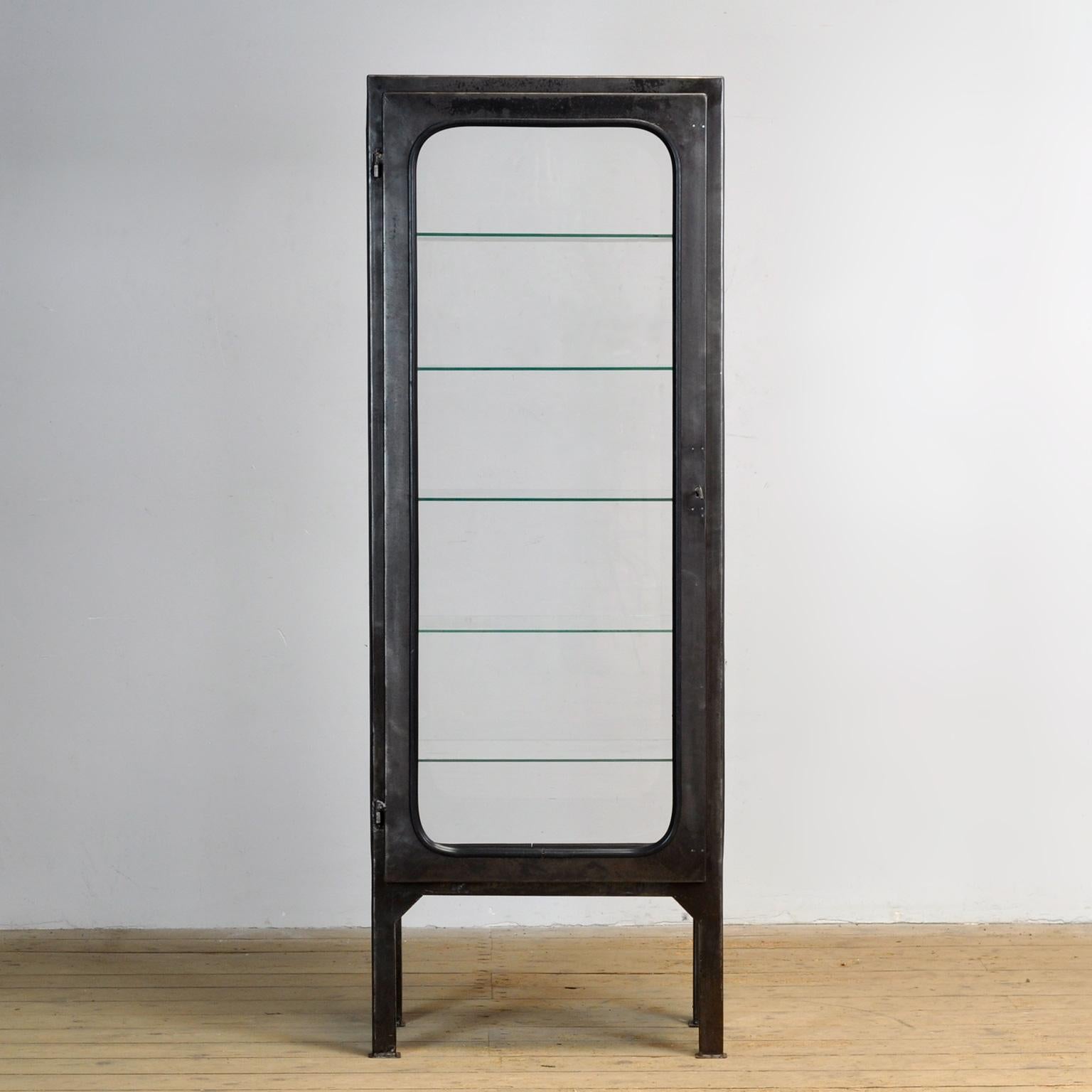Composé d'acier et de verre qui est serré dans l'acier par une bande de caoutchouc. Le meuble date des années 1970 et a été fabriqué en Hongrie. La vitrine a été décapée jusqu'au métal et finie avec une laque transparente. Livré avec 5 étagères en