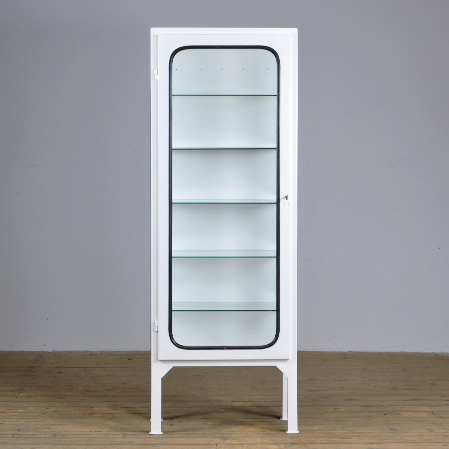 This medicine cabinet was designed in the 1970s and produced in 1975 in Hungary. It is made from steel and antique glass, with the glass panes held in place by a black rubber strip. The cabinet features five adjustable glass shelves and a