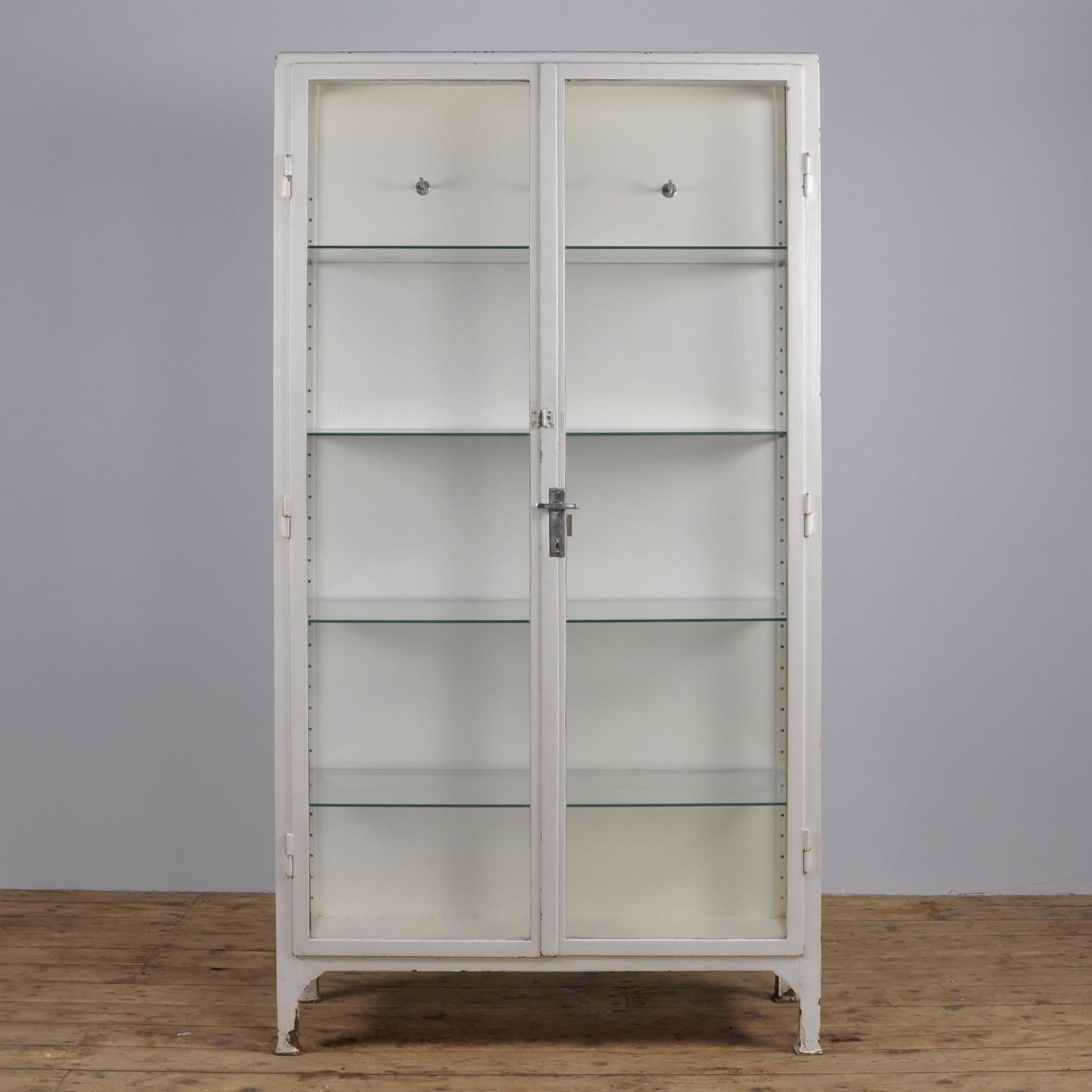 This medicine cabinet was produced in the 1950s in Hungary. The cabinet is made from thick iron and glass. It features four new glass shelves and three clothing hooks.
