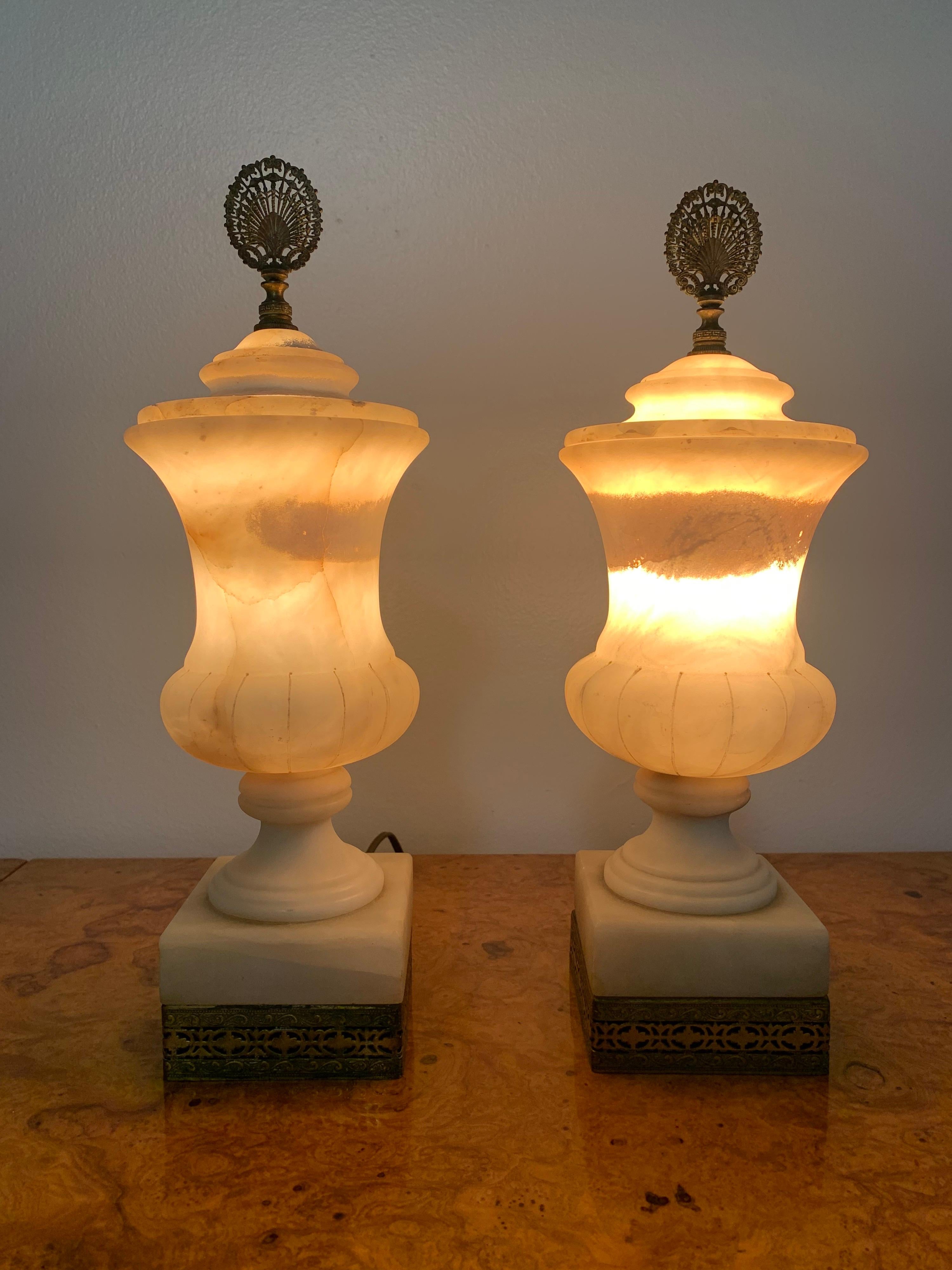 Gorgeous pair of Alabaster lidded urn lamps. Masterfully carved with amazing form. Aging gracefully resulting in a light caramel coloring and bringing. Ornate brass fixtures on the top and bottom accenting the form and color of the urns. 

Hand