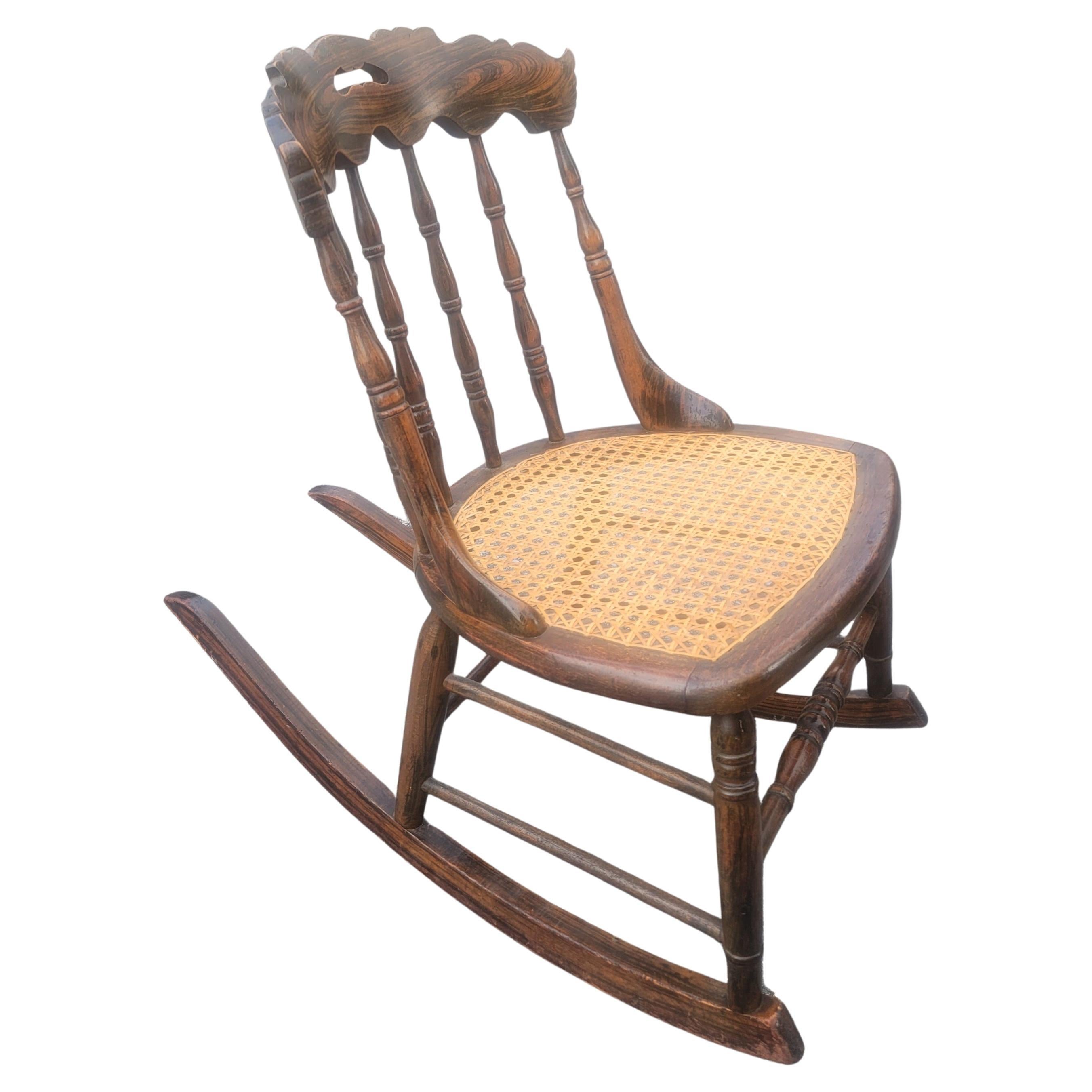 Une exquise chaise à bascule vintage de taille moyenne en noyer et siège de canne en noyer tigré. Des coups de bâton plus récents. Très bon état vintage.