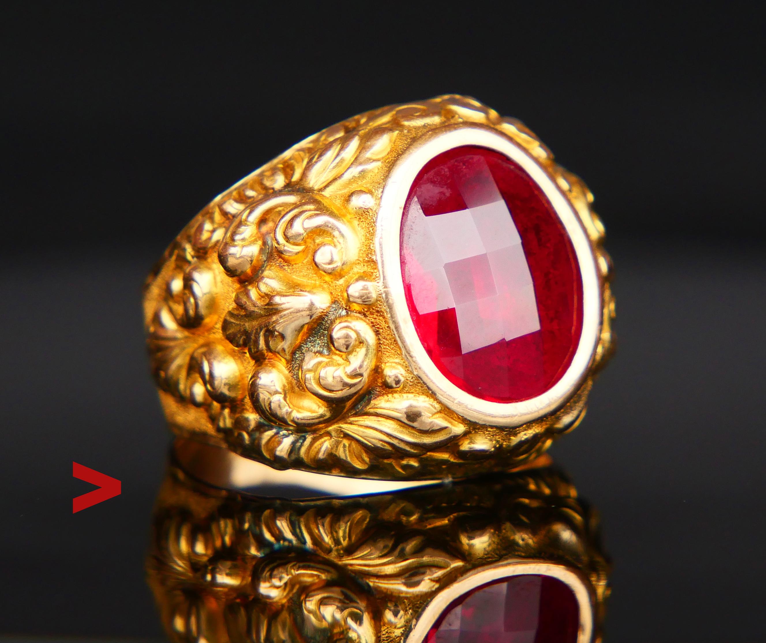 A Ring for Men with cast and engraved floral decorations on wide shoulders adorned with bezel set oval cut and faceted lab-made Red Ruby stone 14 mm x 11 mm with closed back / ca 8 ct.

The design and natural hardness of the Ruby stone of this ring