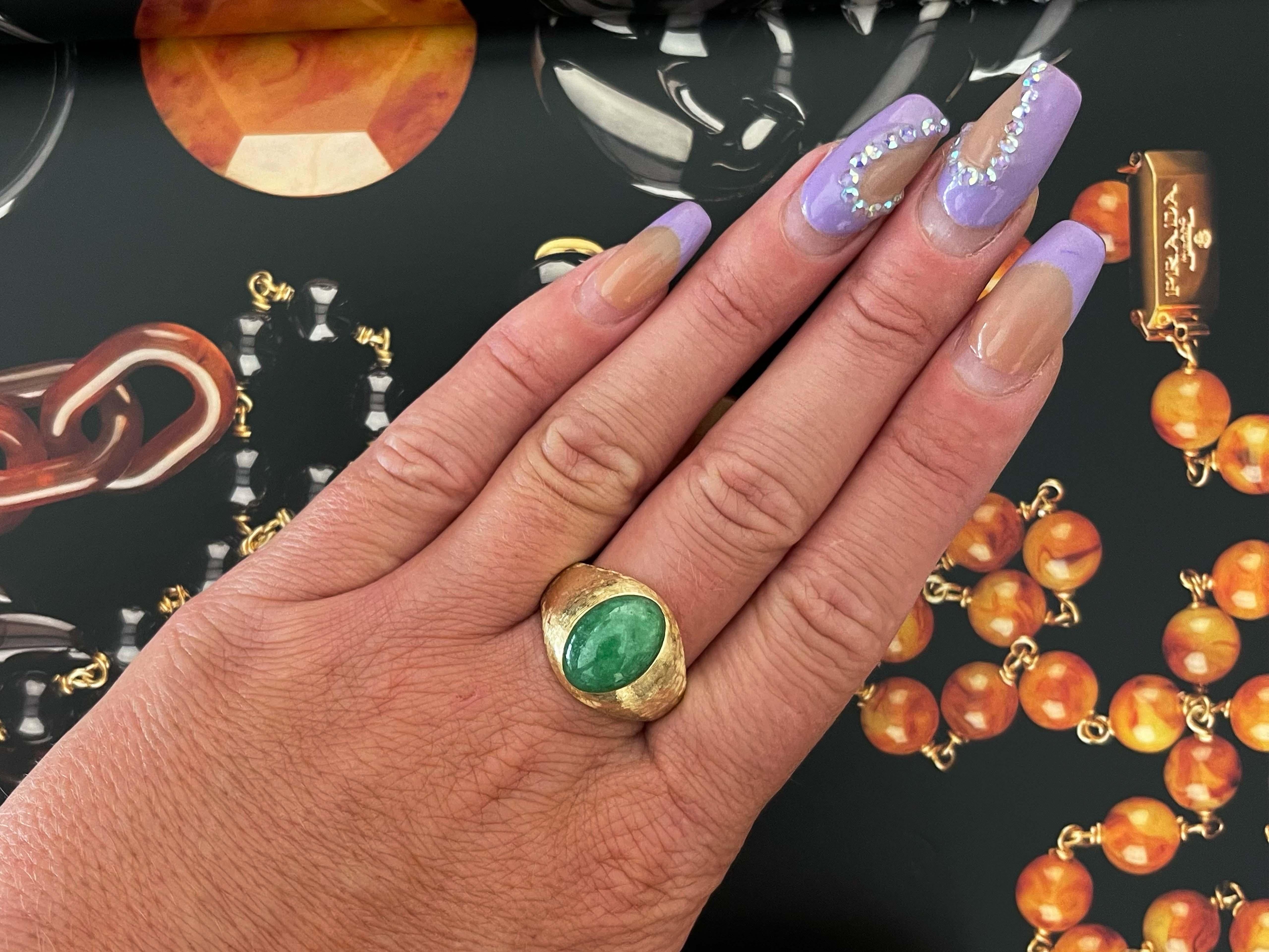 Magnificent vintage oval cabochon green jadeite jade ring, in 14k yellow gold. The beautiful mottled green Jade is bezel set and measures approximately 14.43 mm x 9.96mm x 5.54 mm. The ring has a tapered shank with a textured design. The ring is