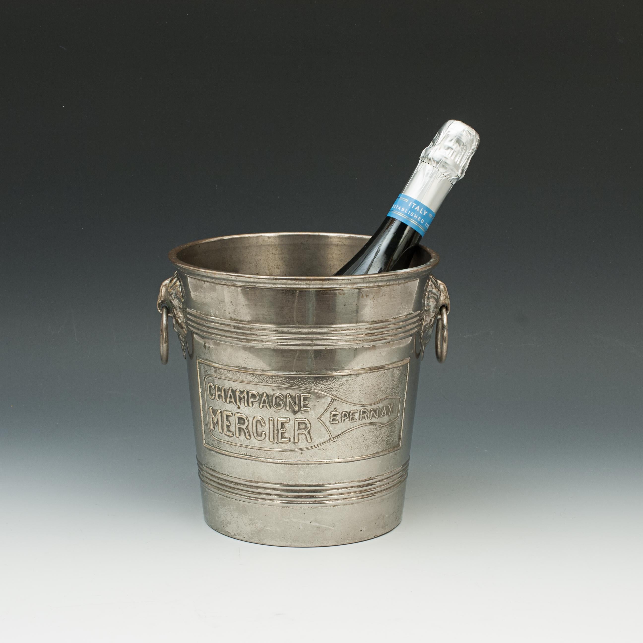 Vintage Champagne ice bucket.
A nice and well used good quality Mercier Champagne ice bucket. The metal bucket is plated and polished with drop ring handles. The front and back have applied embossed metal Champagne bottle reading 'CHAMPAGNE MERCIER
