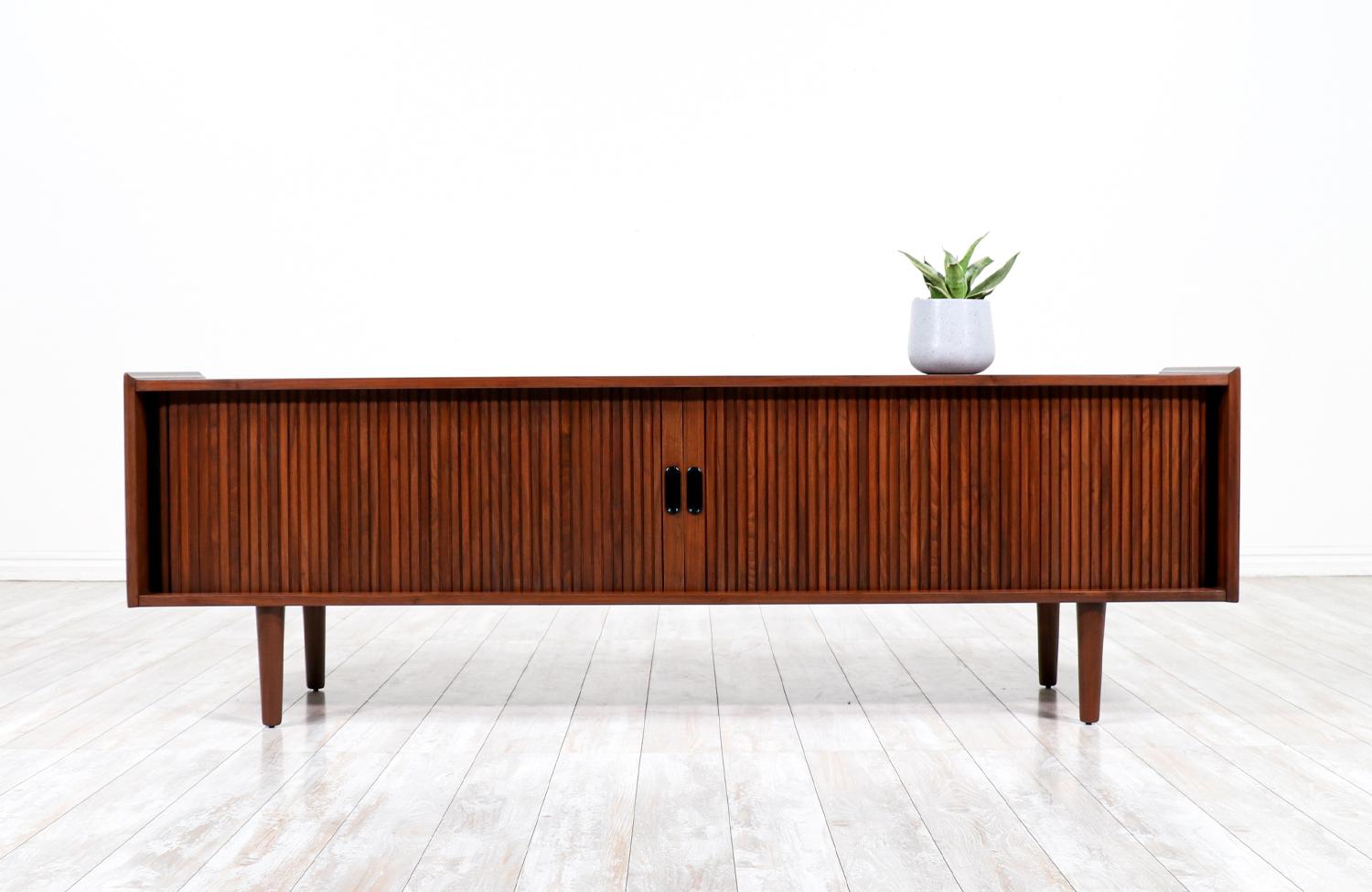 Spacious tambour-door credenza designed by Merton L. Gershun for Dillingham in the United States circa 1960’s. Crafted with walnut wood and newly refinished by our skilled craftsmen, this credenza features two tambour doors with recessed pulls that